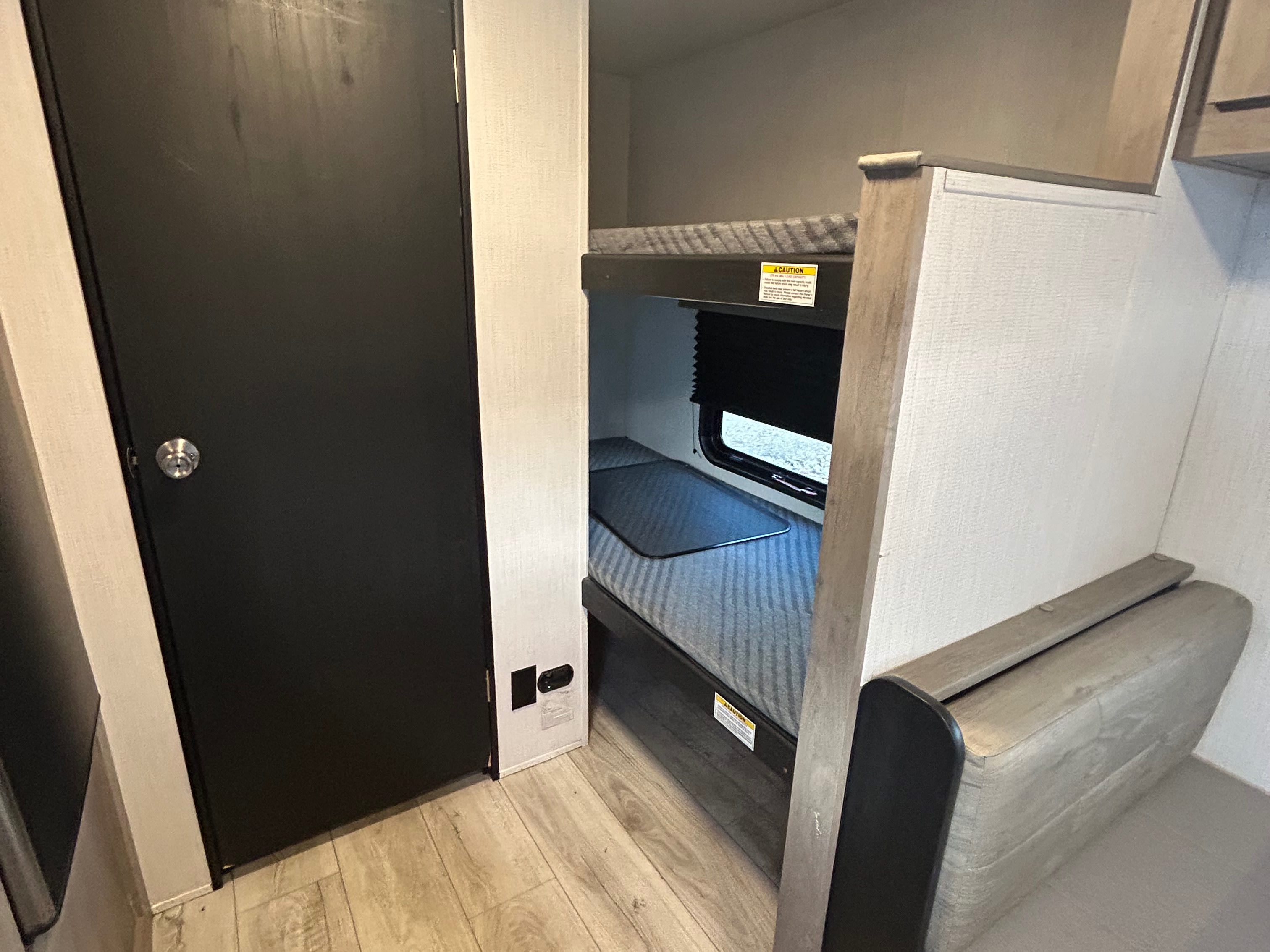 Inside this RV rental: a dark door, stacked bunk beds with mattresses & a window, plus floor outlets for your journey.. Cruiser RV A-17BH Avenir 2024