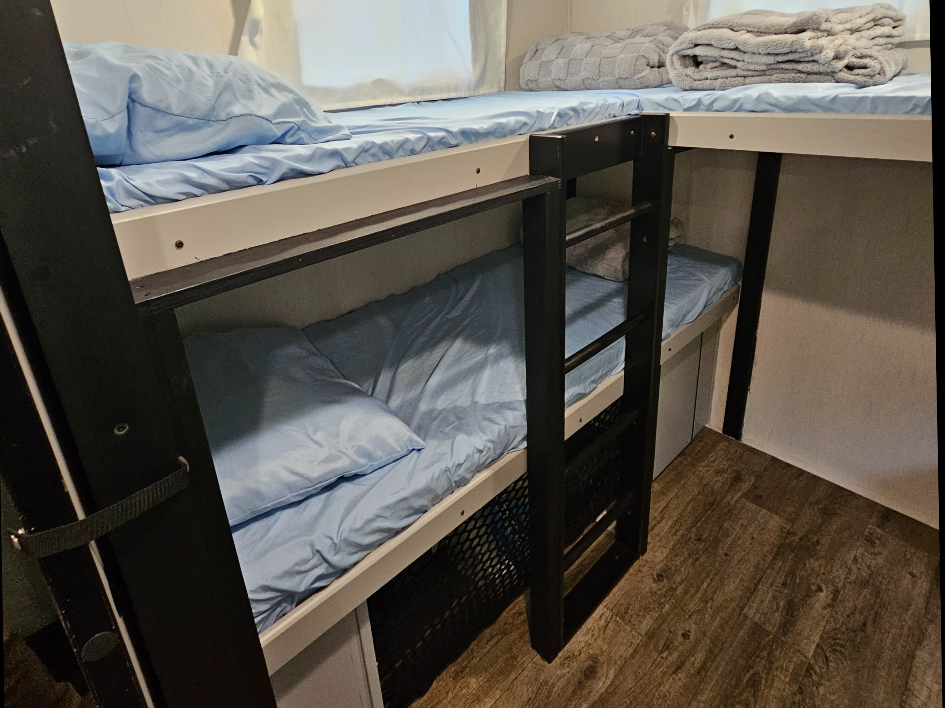 RV rental bunk beds: compact sleeping area with blue sheets, pillows, and grey blankets, accessible by a black ladder.. Forest River Vibe 2022