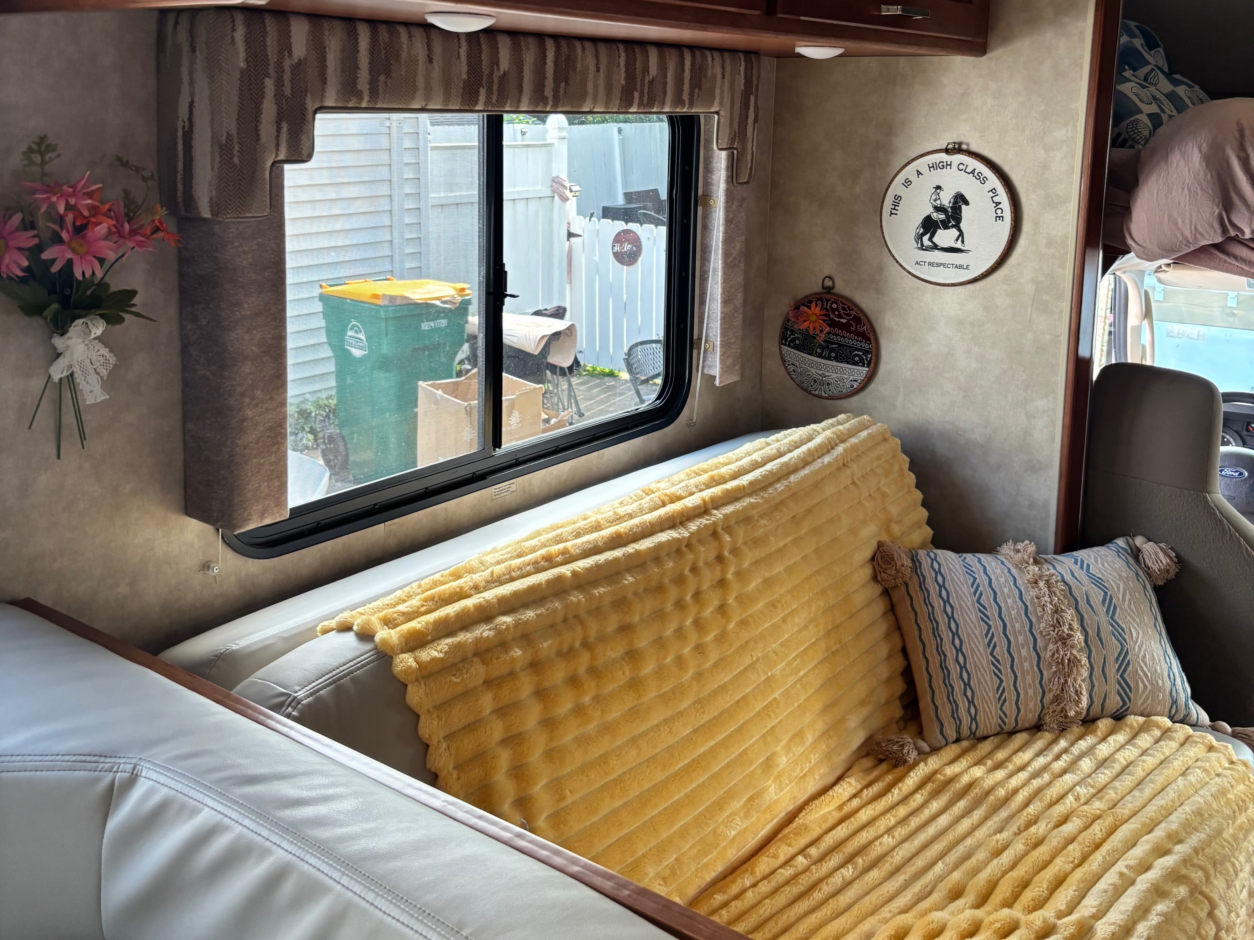This cozy RV rental living area features a sofa with a yellow blanket, patterned pillow, and window views. Wall decor adds character.. Winnebago Minnie Winnie 2019