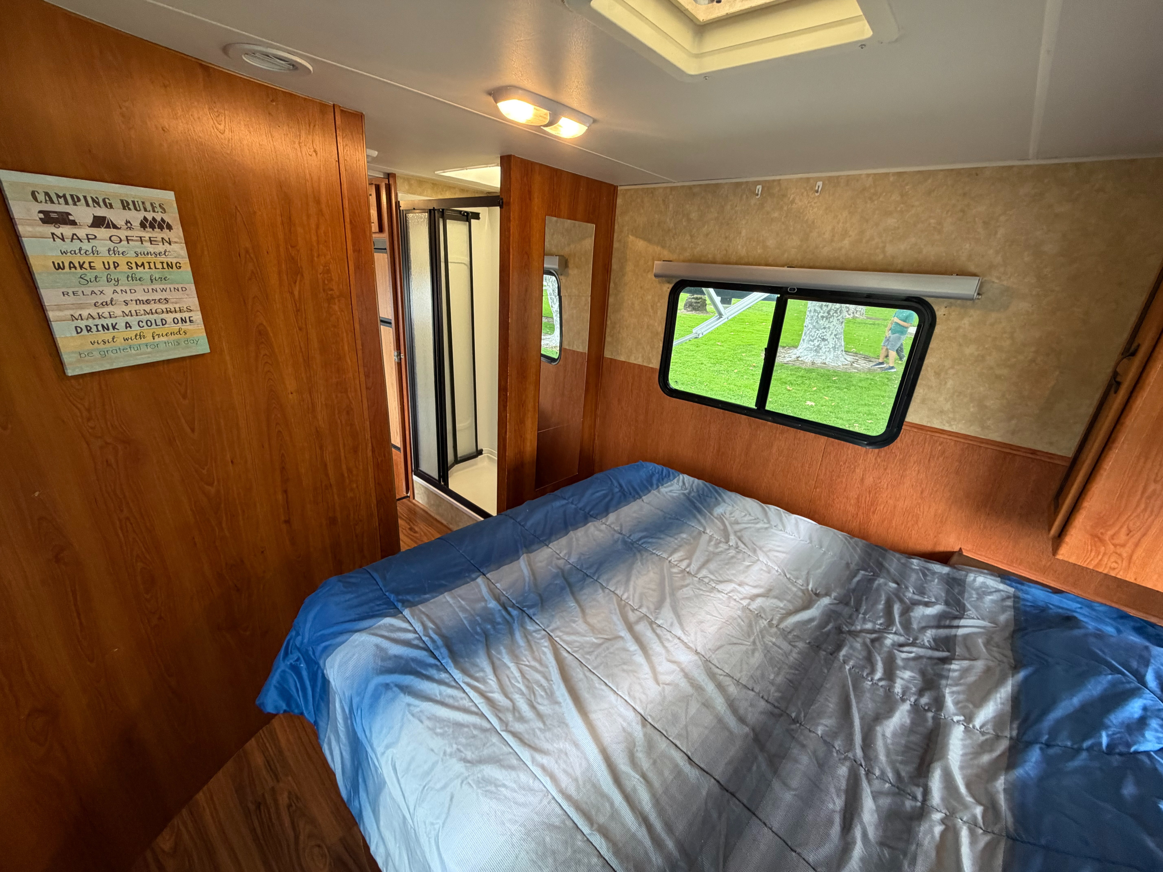 Cozy RV rental bedroom featuring a blue and white comforter, window view of trees, and "Camping Rules" decor.. Coachmen Freelander 2010