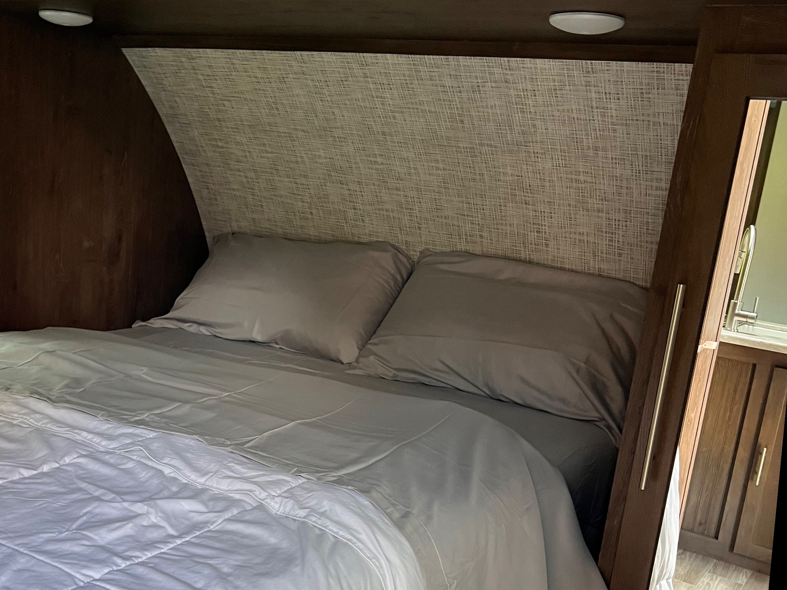 Comfortable RV rental bedroom with a neatly made bed, grey sheets, white comforter, and textured headboard.. Forest River Salem Hemisphere Lite 2019