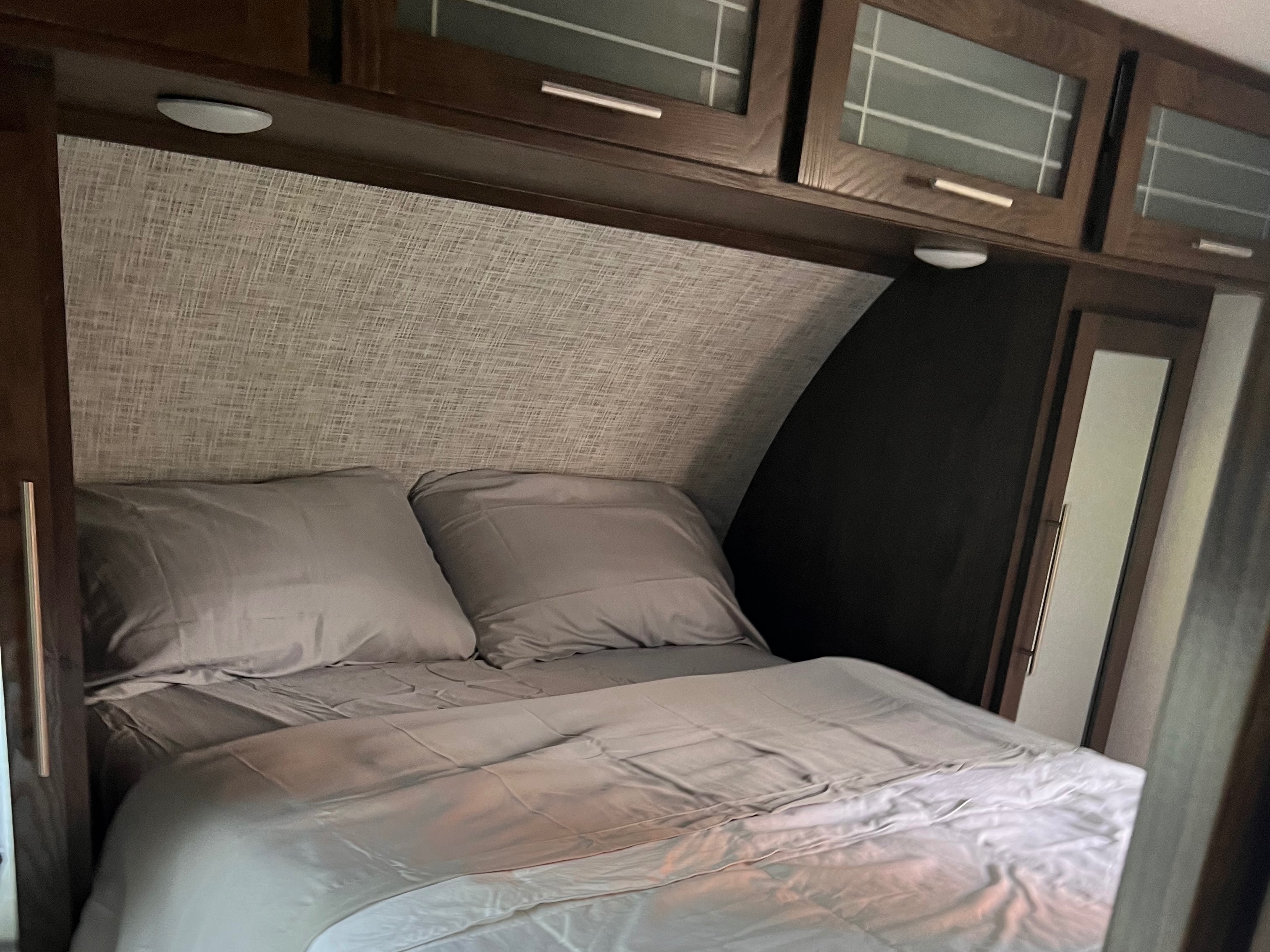 Cozy RV rental bedroom features a gray bed, textured headboard, dark wood cabinets with lights, and mirrored wardrobe.. Forest River Salem Hemisphere Lite 2019