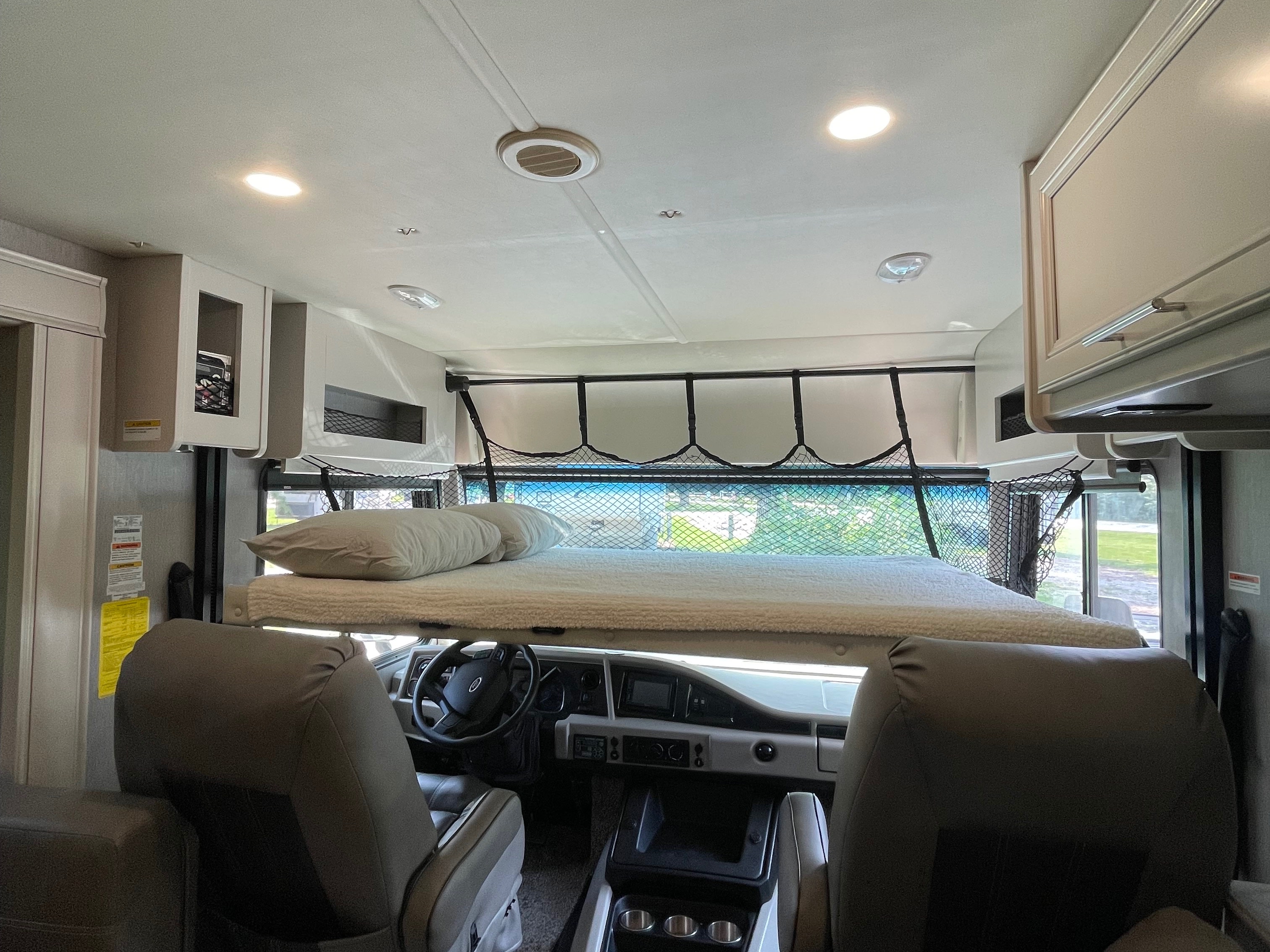 Inside an rv rental: a cozy overhead bunk with safety netting above the driver's area, visible dashboard and seats.. Flair-Fleetwood Flair-Fleetwood Motorhome 2022