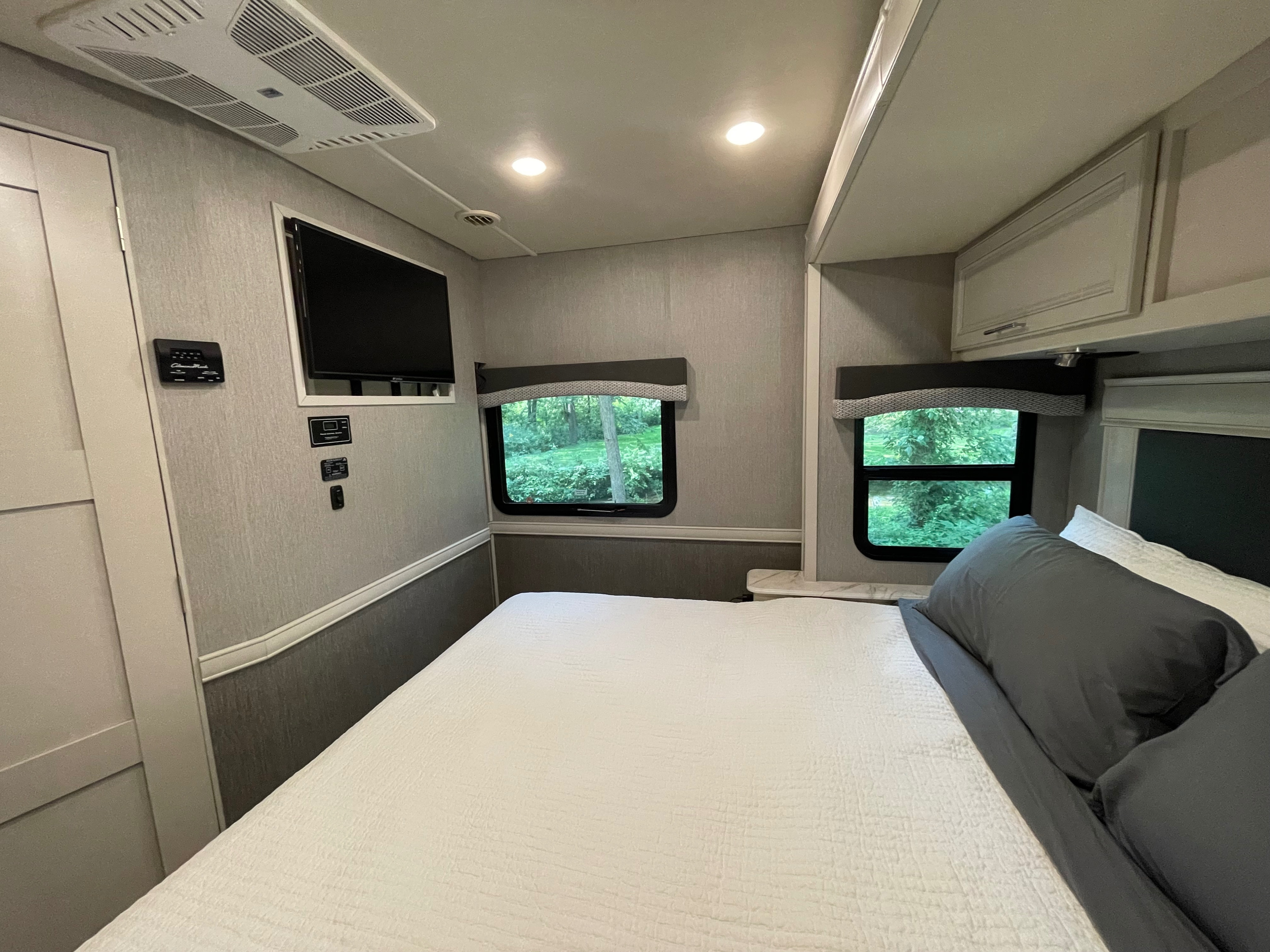Modern RV rental bedroom featuring a comfortable bed, windows with nature views, AC, TV, and convenient controls.. Flair-Fleetwood Flair-Fleetwood Motorhome 2022