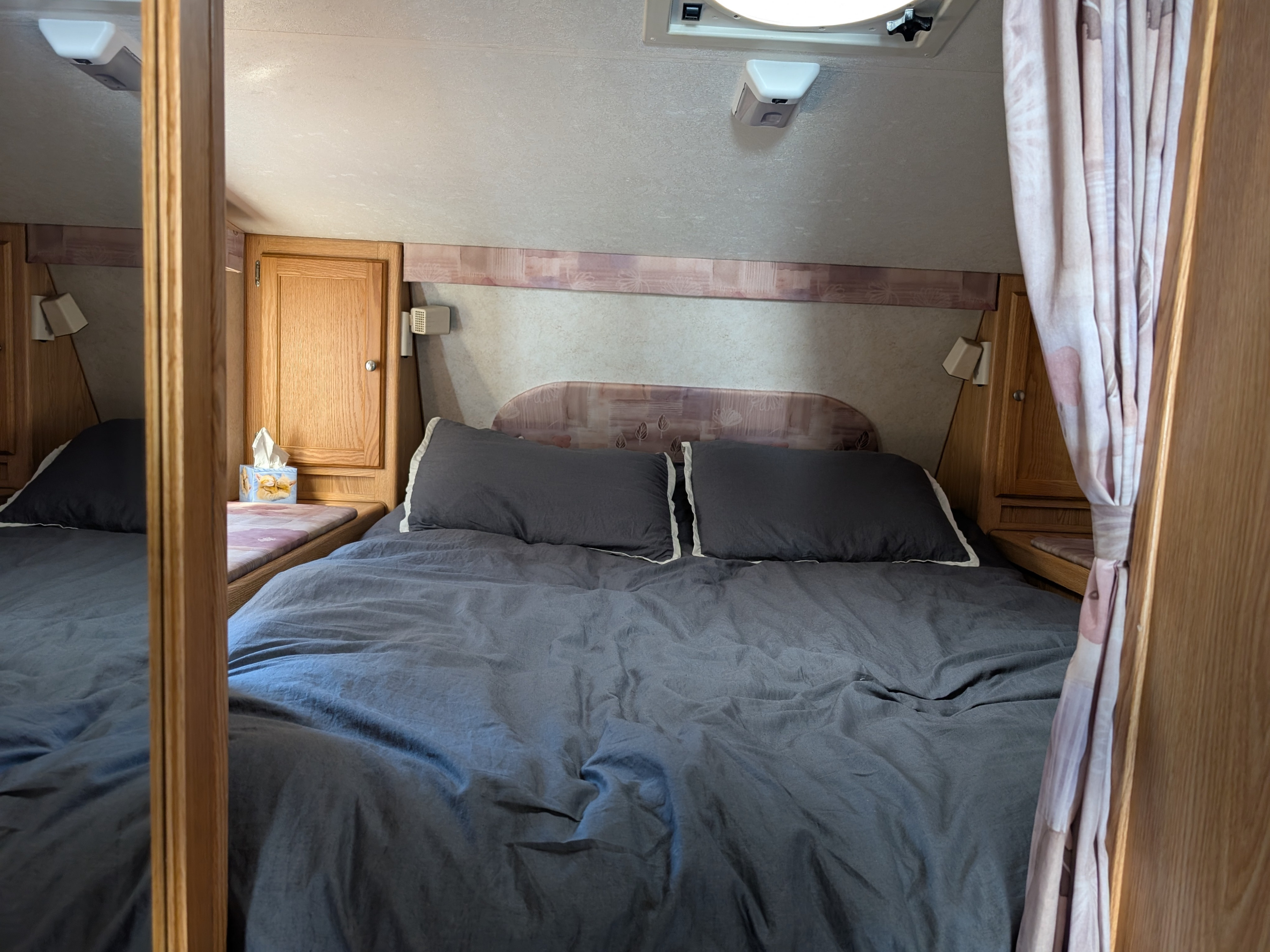 Cozy bedroom in an RV rental with dark grey bedding, wooden cabinets, and a patterned headboard. Features a ceiling vent and wall lights.. Dodge Dodge 1 Ton Pu 2014