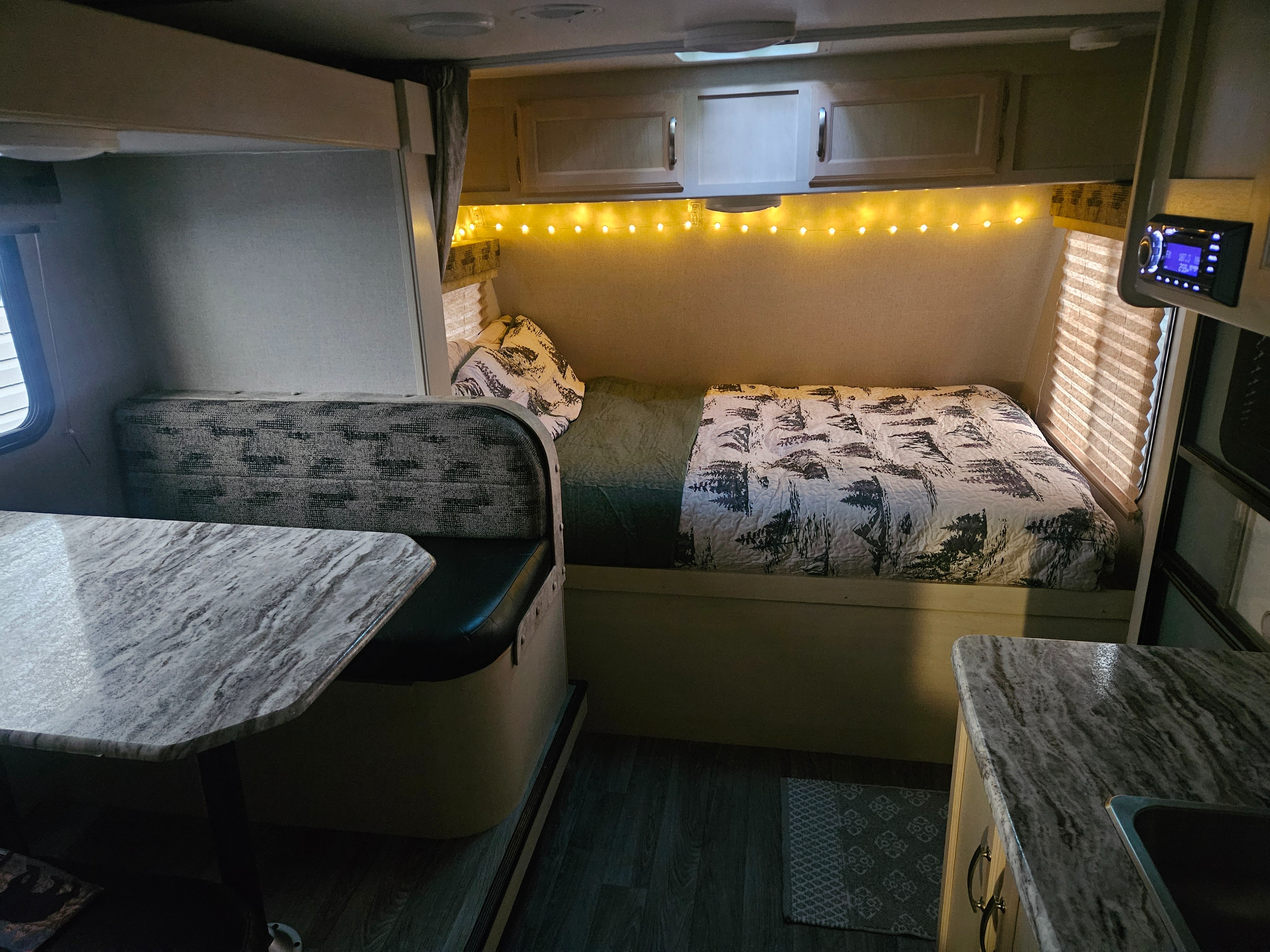 This RV rental interior features a cozy bed with string lights, dinette, and kitchen area for comfortable travel.. Winnebago 2100bh 2019