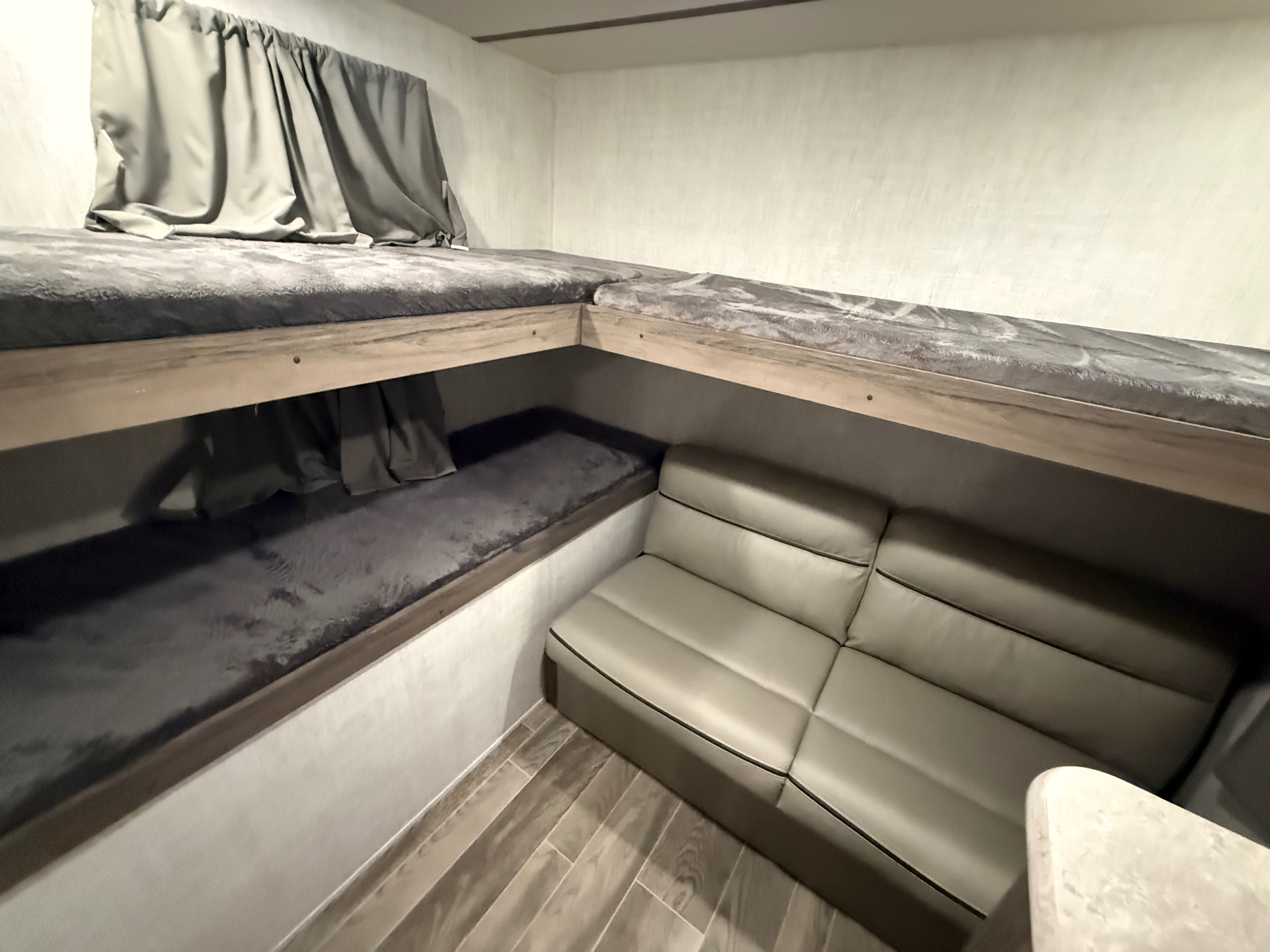Cozy bunk beds with curtains and a comfortable sofa in this RV rental's interior, ideal for family travel.. Gulf Stream Ameri-Lite 2021