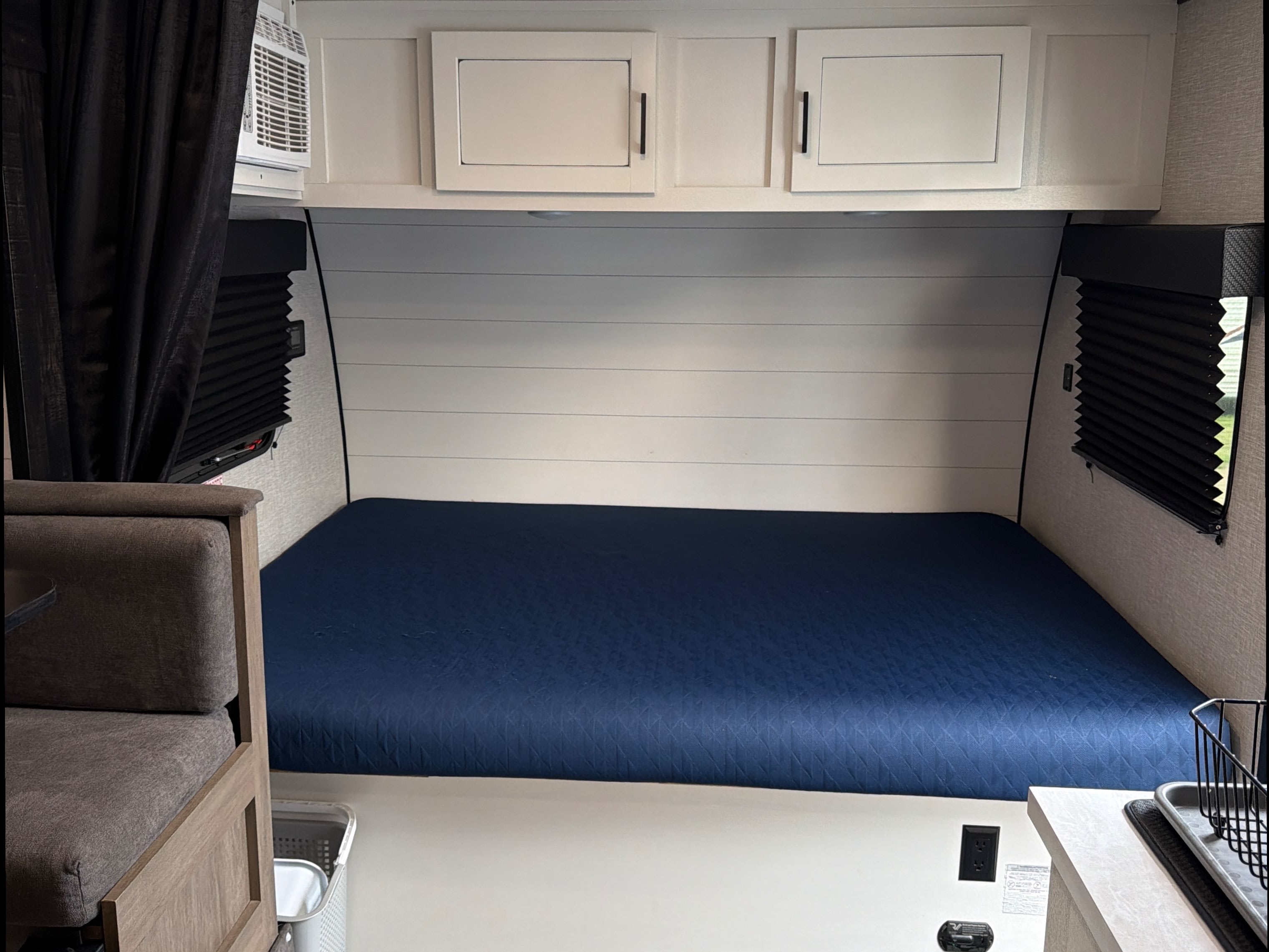 This cozy RV rental interior showcases a blue bed, white cabinets, and side windows with blinds, perfect for travel.. Jayco Jay Flight SLX 2024