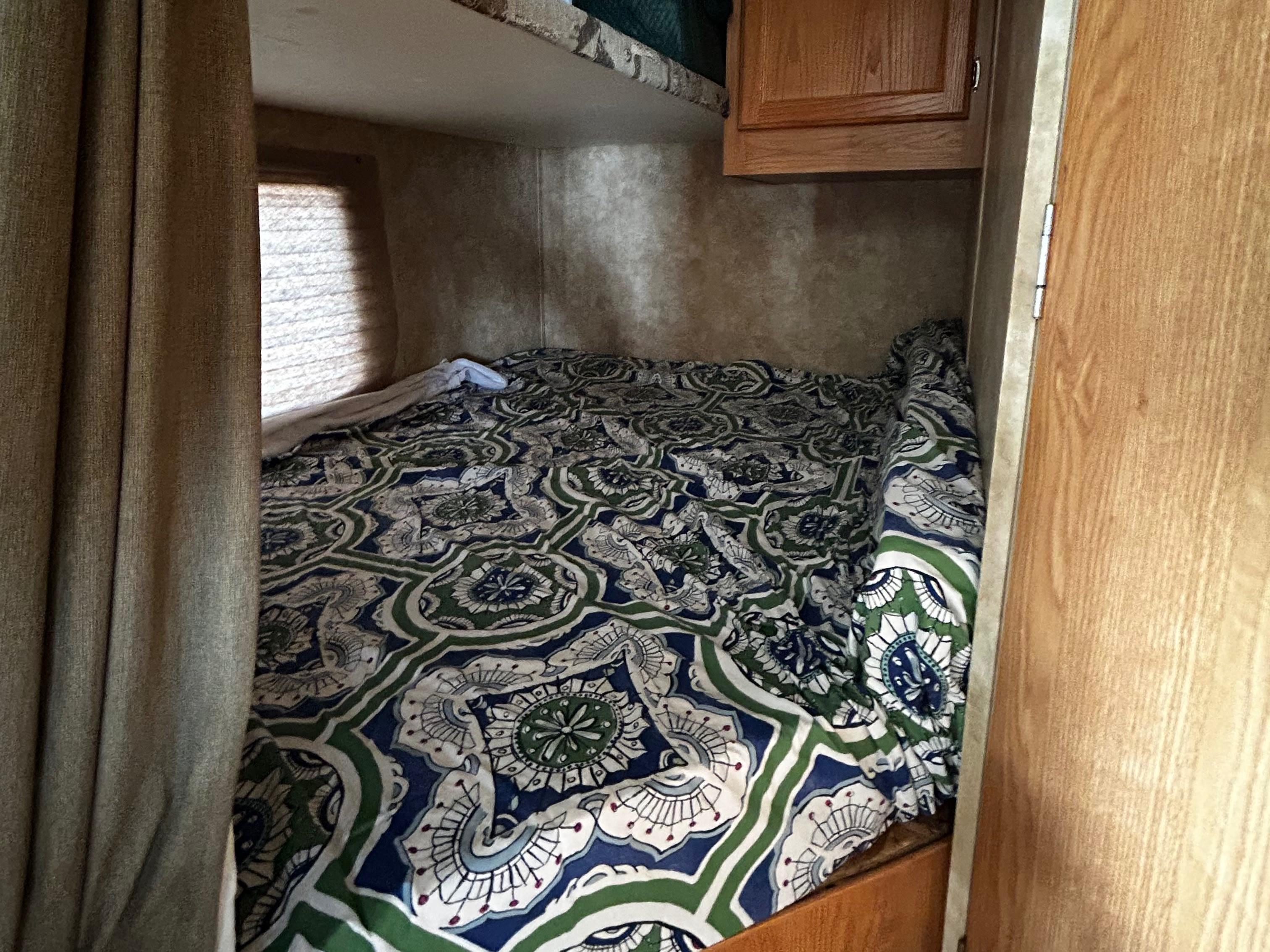 Inside an RV rental: a cozy bed with a vibrant patterned comforter, window, and cabinet. Ideal camper sleeping space.. Coachmen Spirit of America 2009