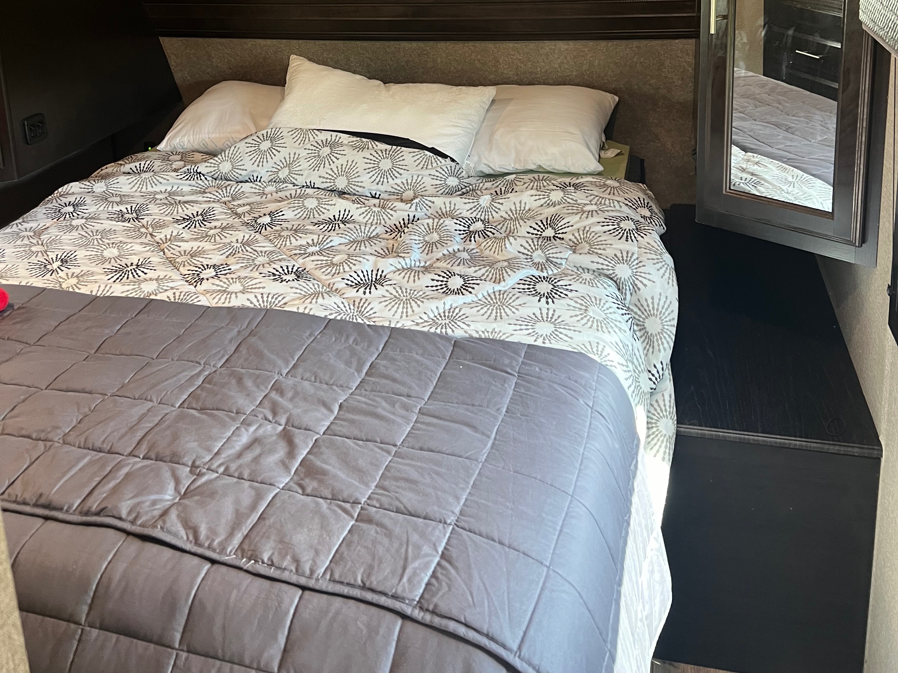 A cozy, made bed with patterned comforter and pillows in an rv rental bedroom, featuring dark wood cabinetry.. Jayco Eagle HT 2020