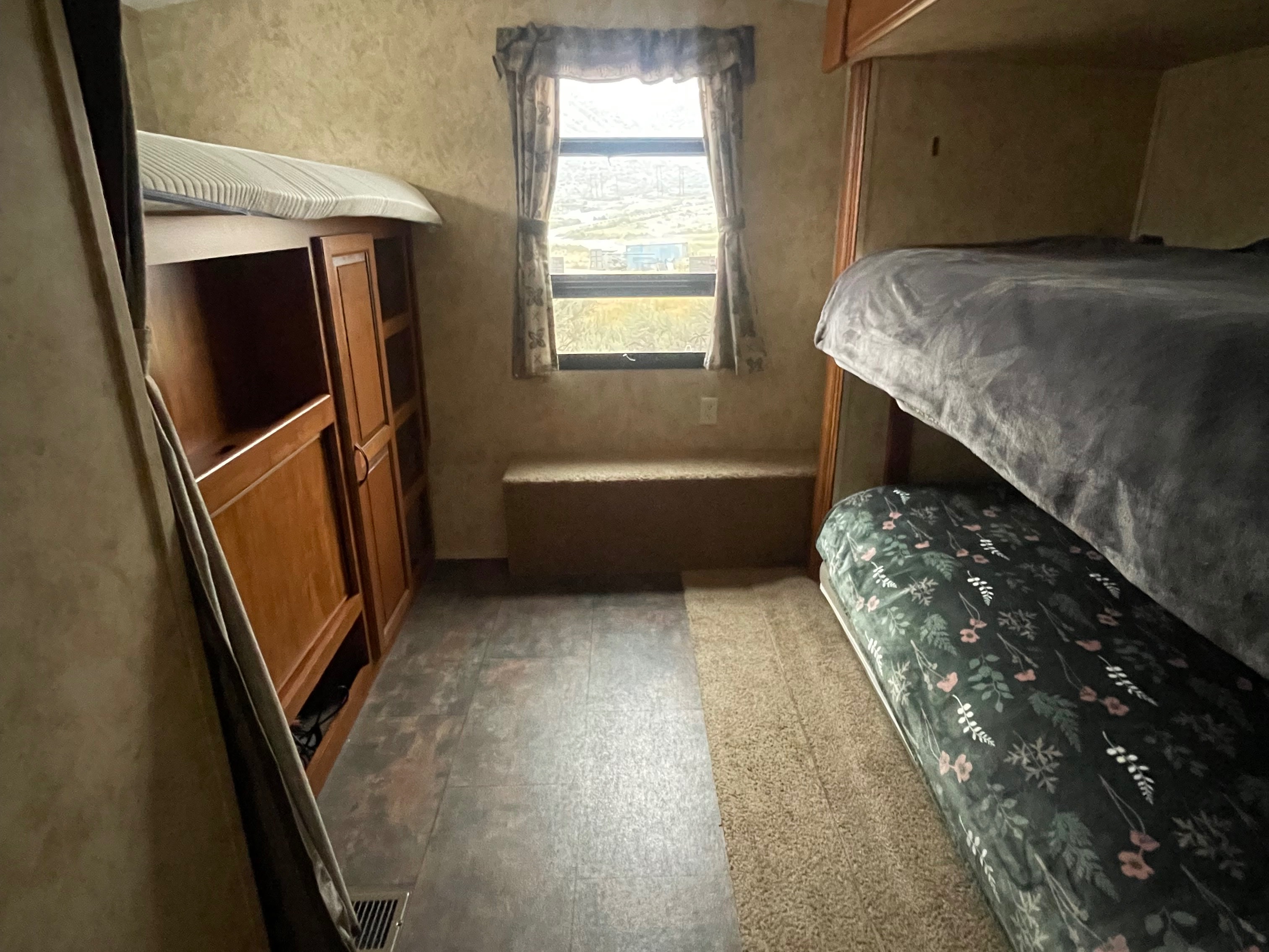 This rv rental bunk room features two bunk beds, a wooden cabinet, a window with curtains, and built-in bench storage.. Keystone RV Bullet Premier Ultra 2010
