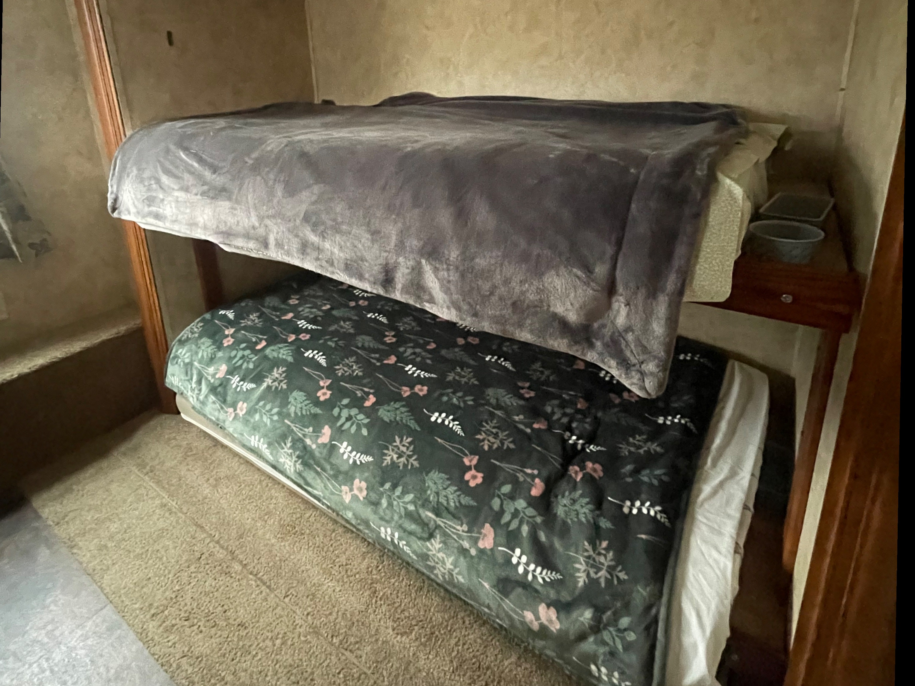 Cozy bunk beds in an RV rental. Top bunk has a gray blanket, bottom has a dark floral blanket.. Keystone RV Bullet Premier Ultra 2010