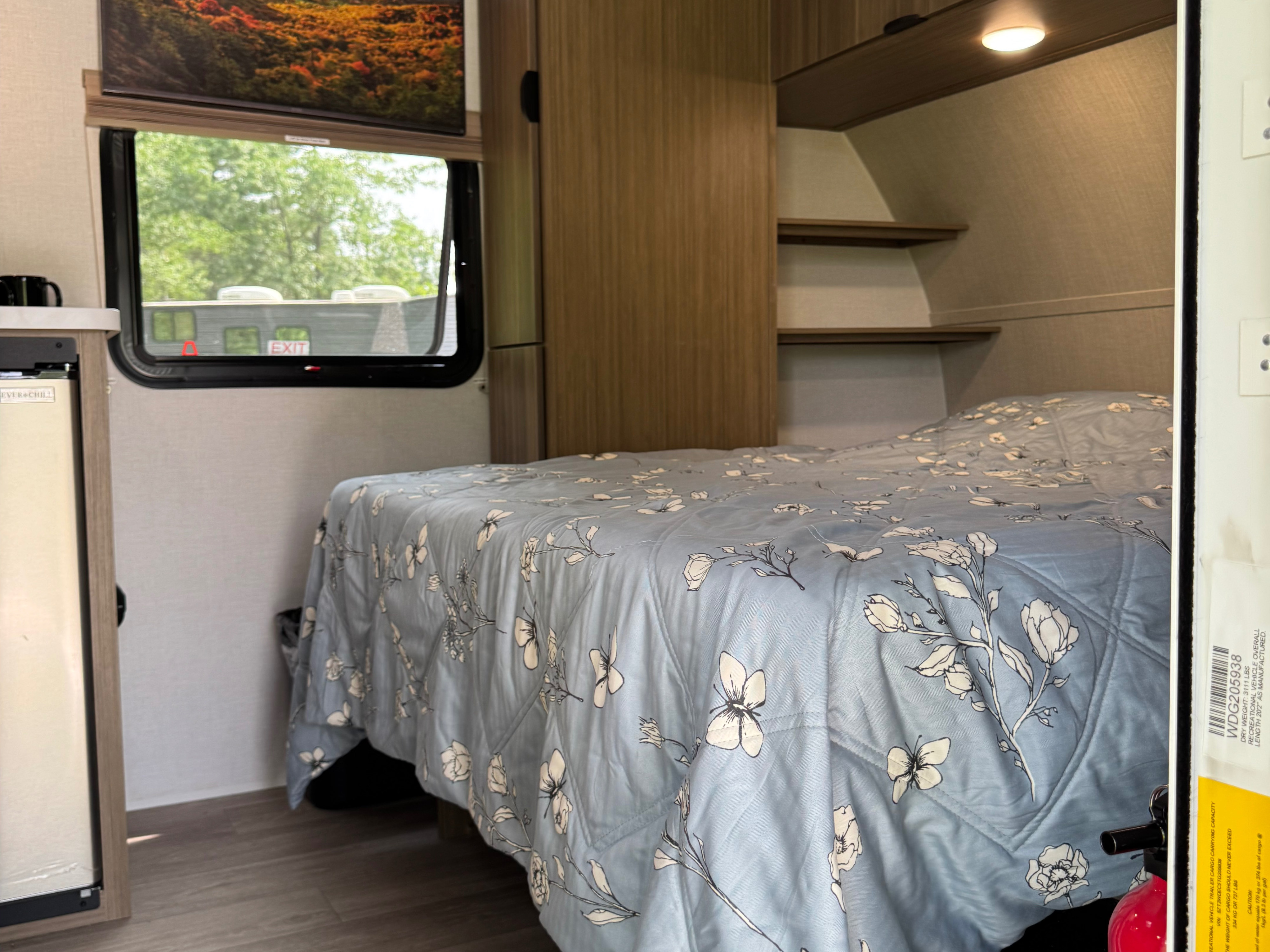 Cozy RV rental bedroom with a floral comforter, window view, and compact fridge, perfect for your next adventure.. Forest River Wildwood FSX 2026