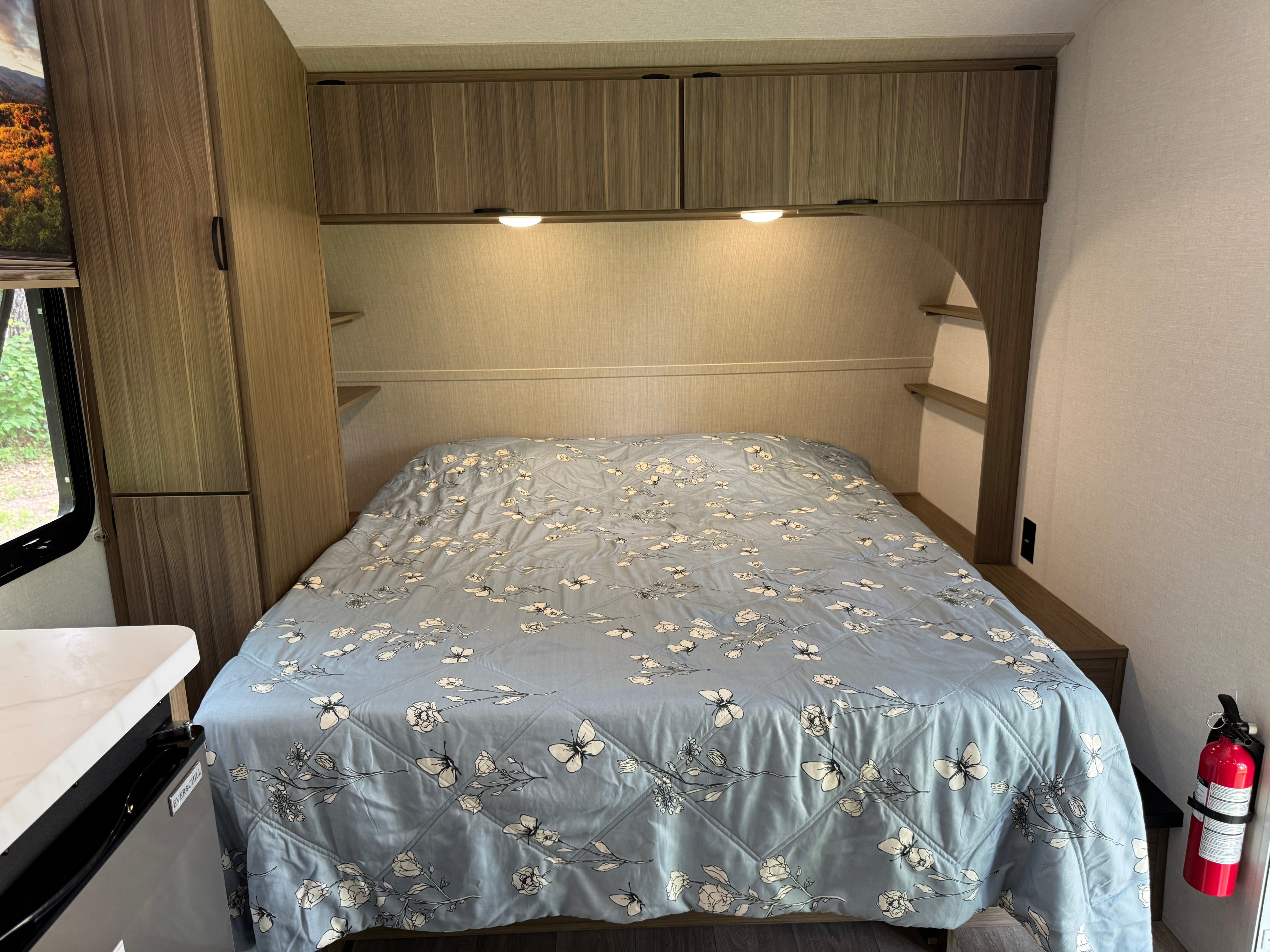 This RV rental bedroom features a comfy bed with a floral comforter, storage cabinets, and a safety fire extinguisher.. Forest River Wildwood FSX 2026