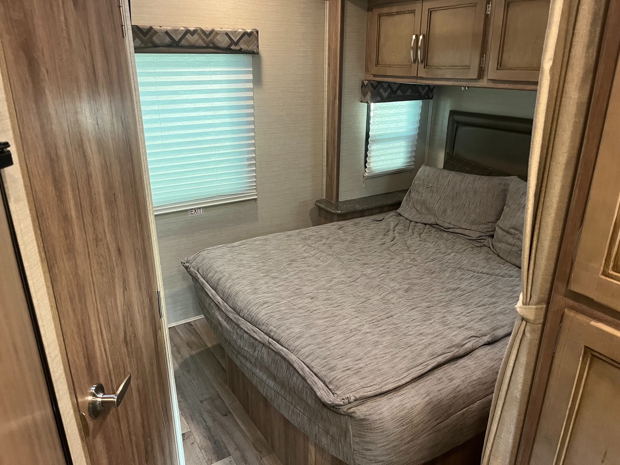Cozy RV rental bedroom interior featuring a comfy bed, window blinds, and practical overhead cabinets for storage.. Jayco Redhawk SE 2019