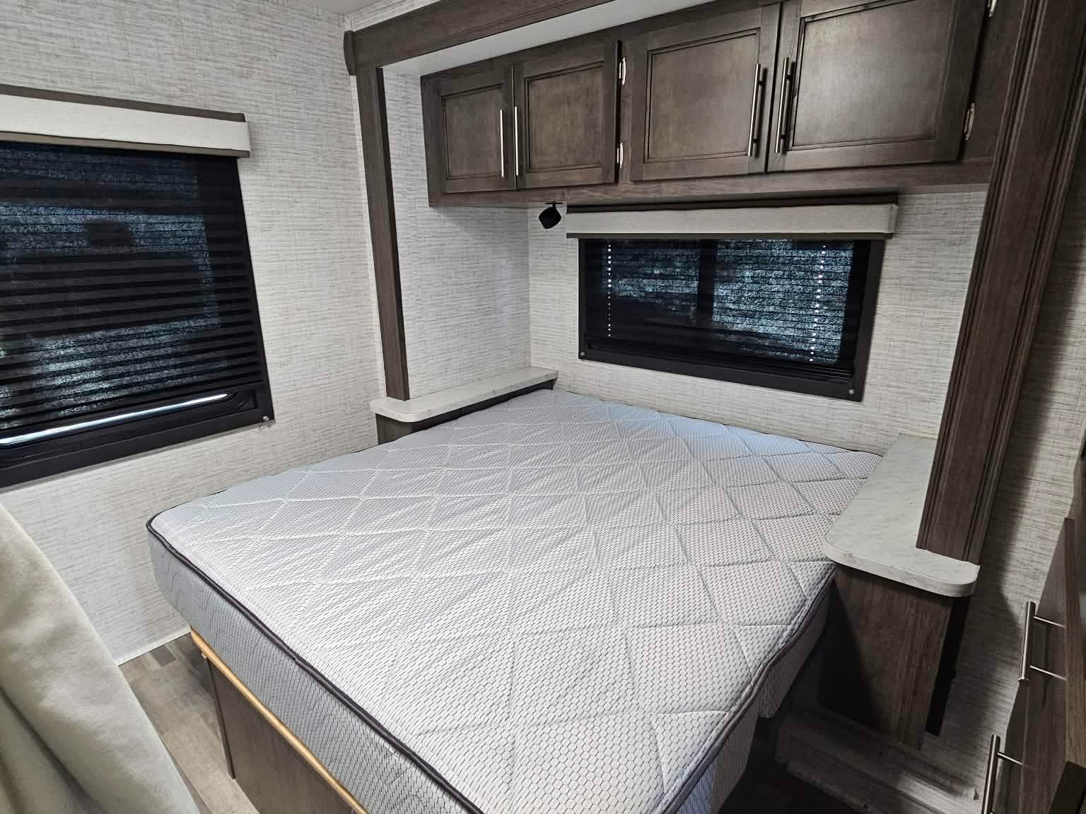 Cozy RV rental bedroom featuring a bed, overhead storage, and shaded windows in this modern camper interior.. Entegra Coach Odyssey SE 2025