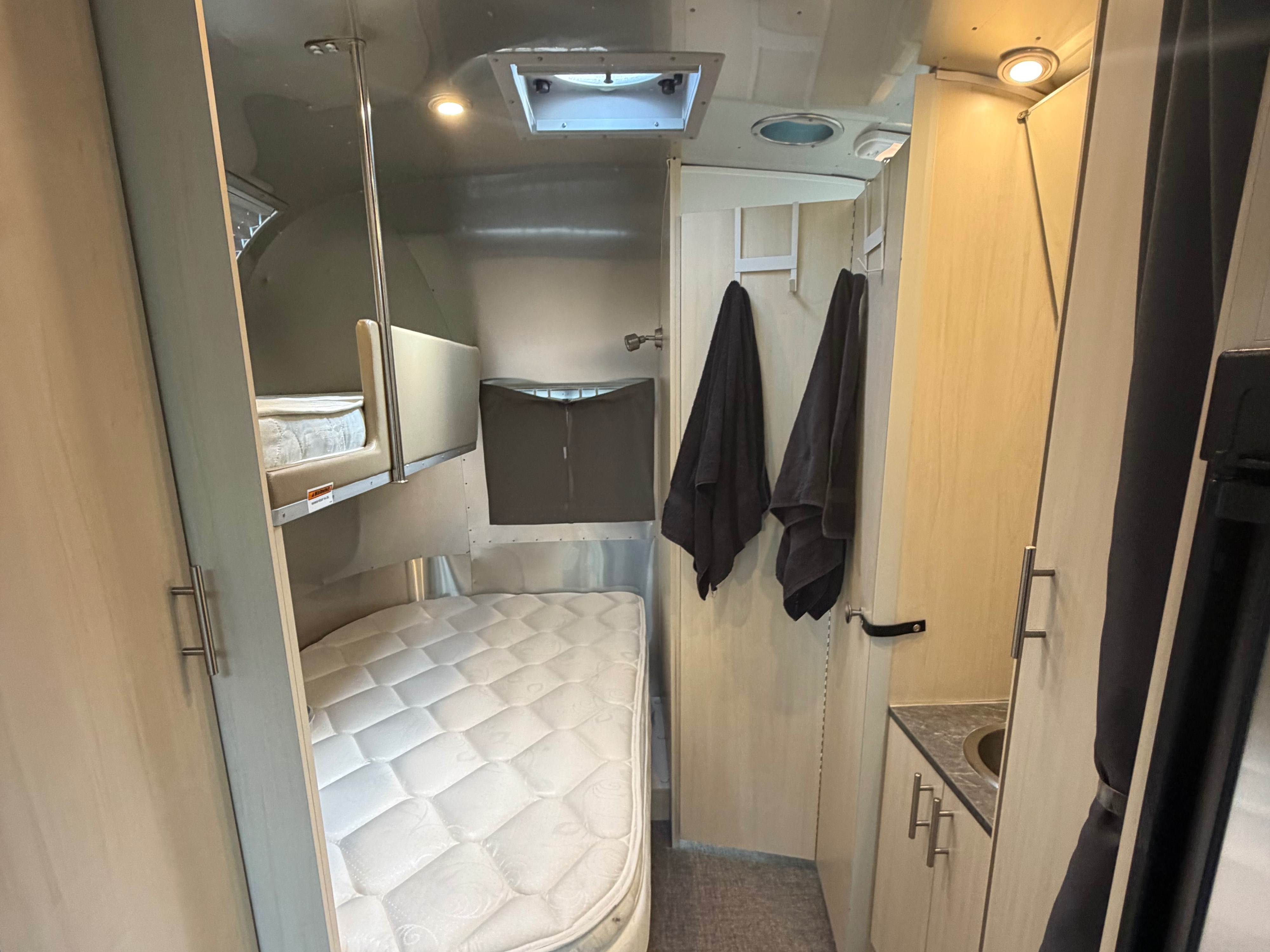 Cozy rv rental interior with bunk beds, a compact bathroom vanity with sink, and hanging towels, ideal for travel.. Airstream Flying Cloud 2021