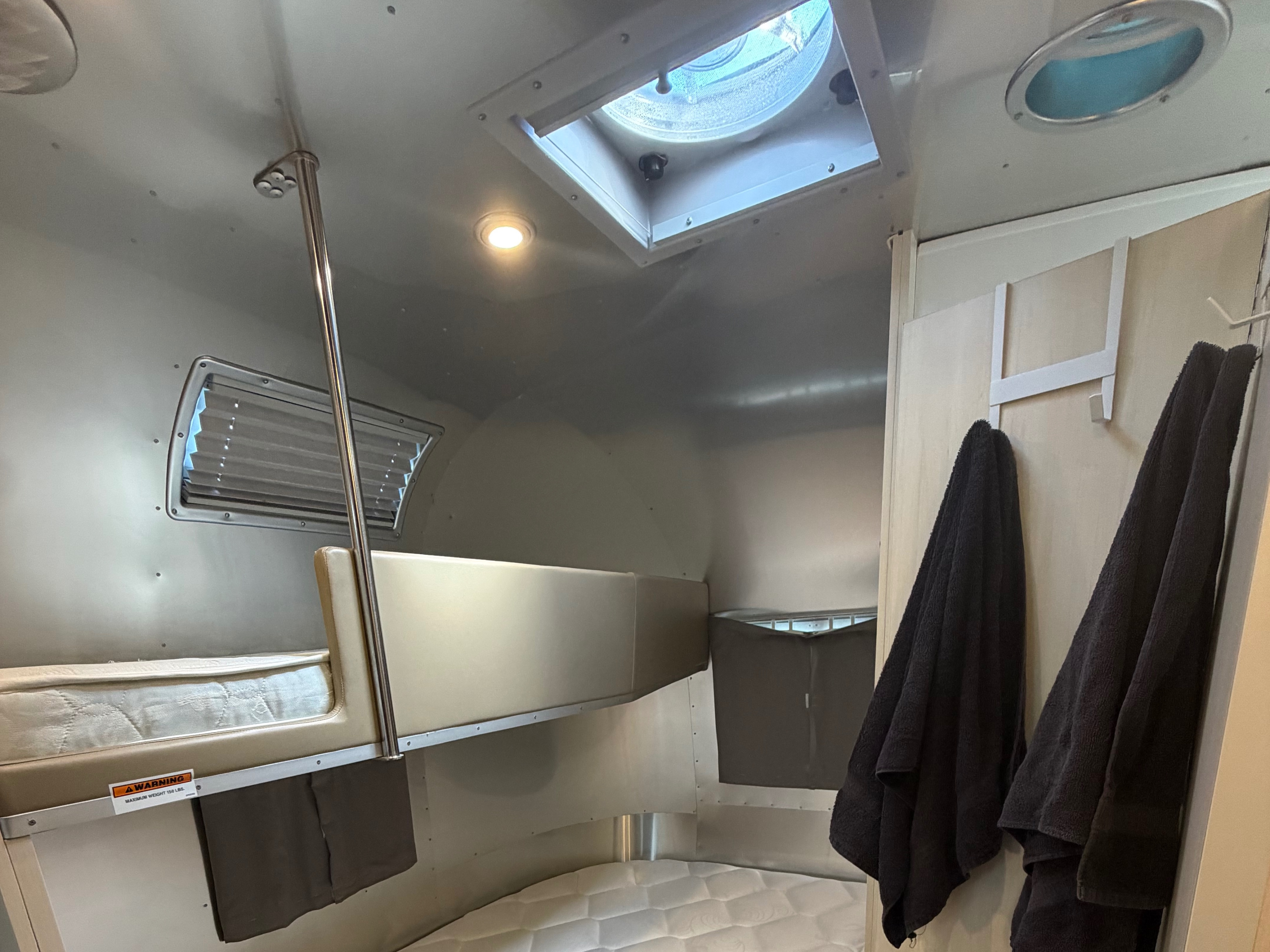 RV rental interior featuring metallic walls, bunk beds, a lower sleeping area, ceiling vent, and hanging towels.. Airstream Flying Cloud 2021