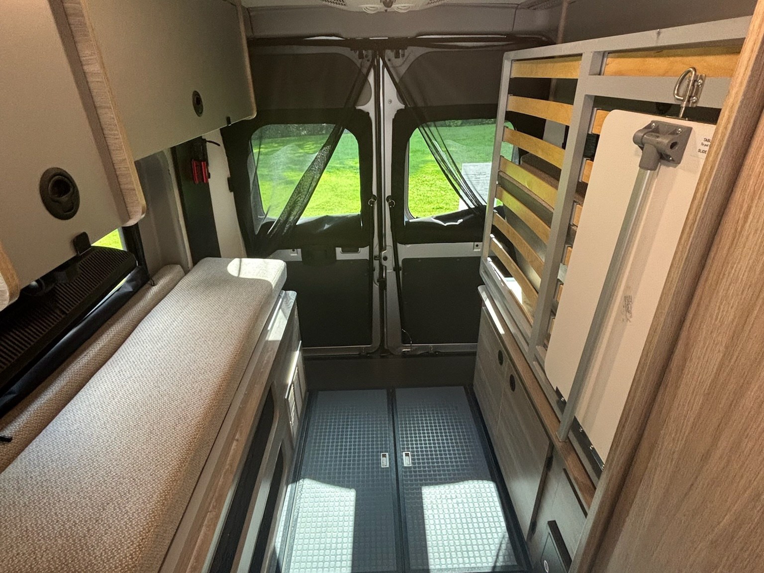 RV rental interior showing a flexible bed/bench on the left, storage, and a fold-down table. Back doors open to nature.. Winnebago Solis 2022