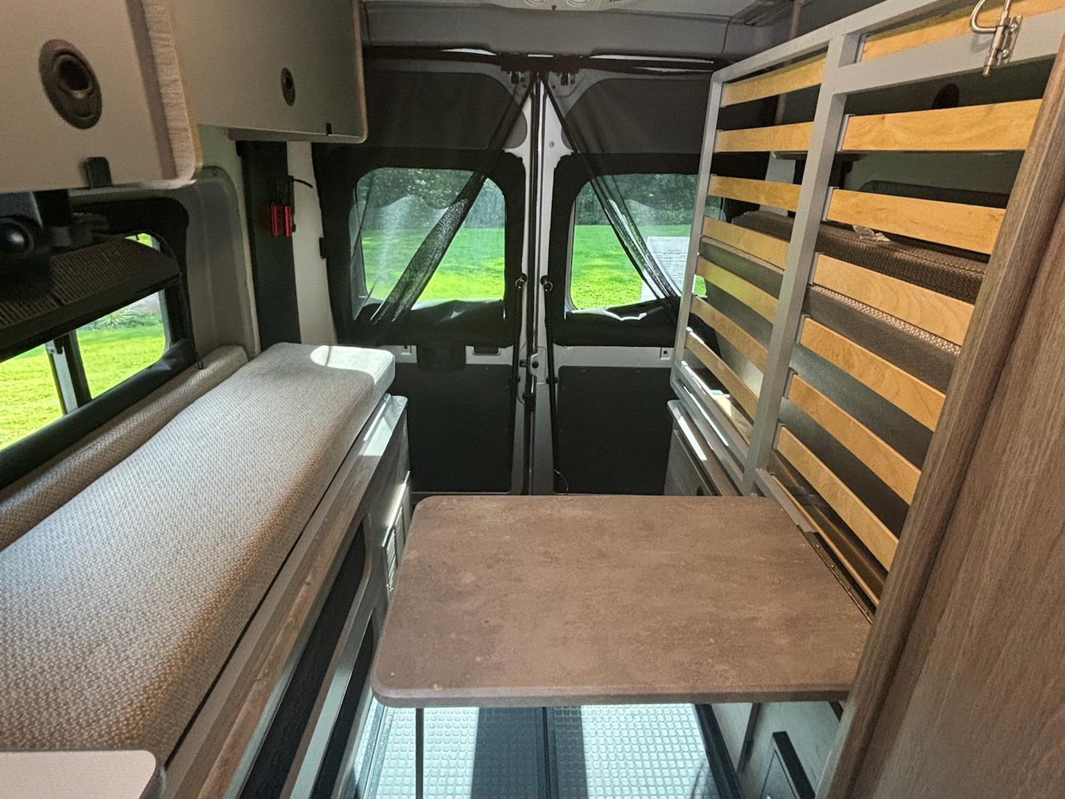 Inside an RV rental: a compact interior features a cushioned bench, a central table, and a slatted bed frame by the screened rear doors.. Winnebago Solis 2022