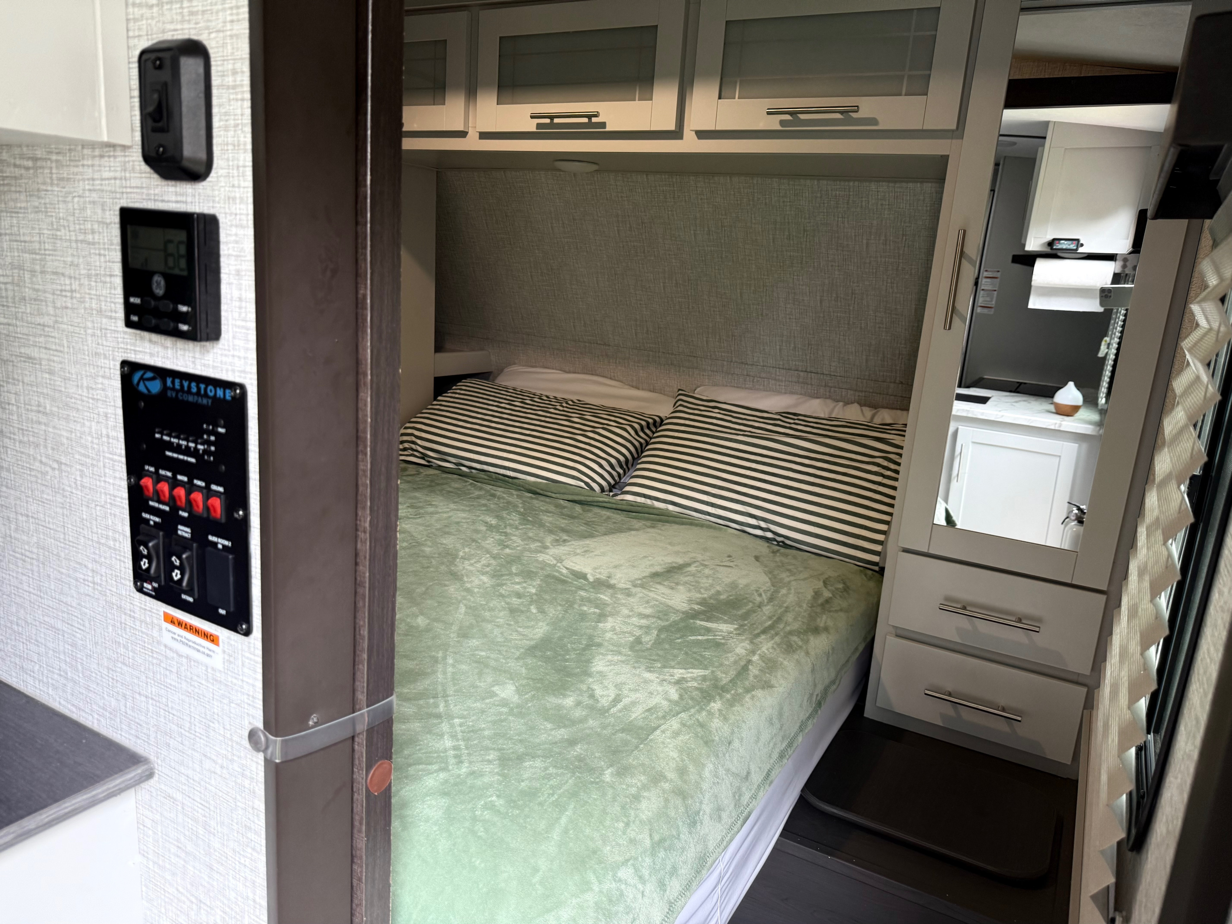 RV rental bedroom with a comfortable bed, mirrored closet, overhead cabinets, and control panel for lighting/water.. Keystone RV Bullet Ultra Lite 2021