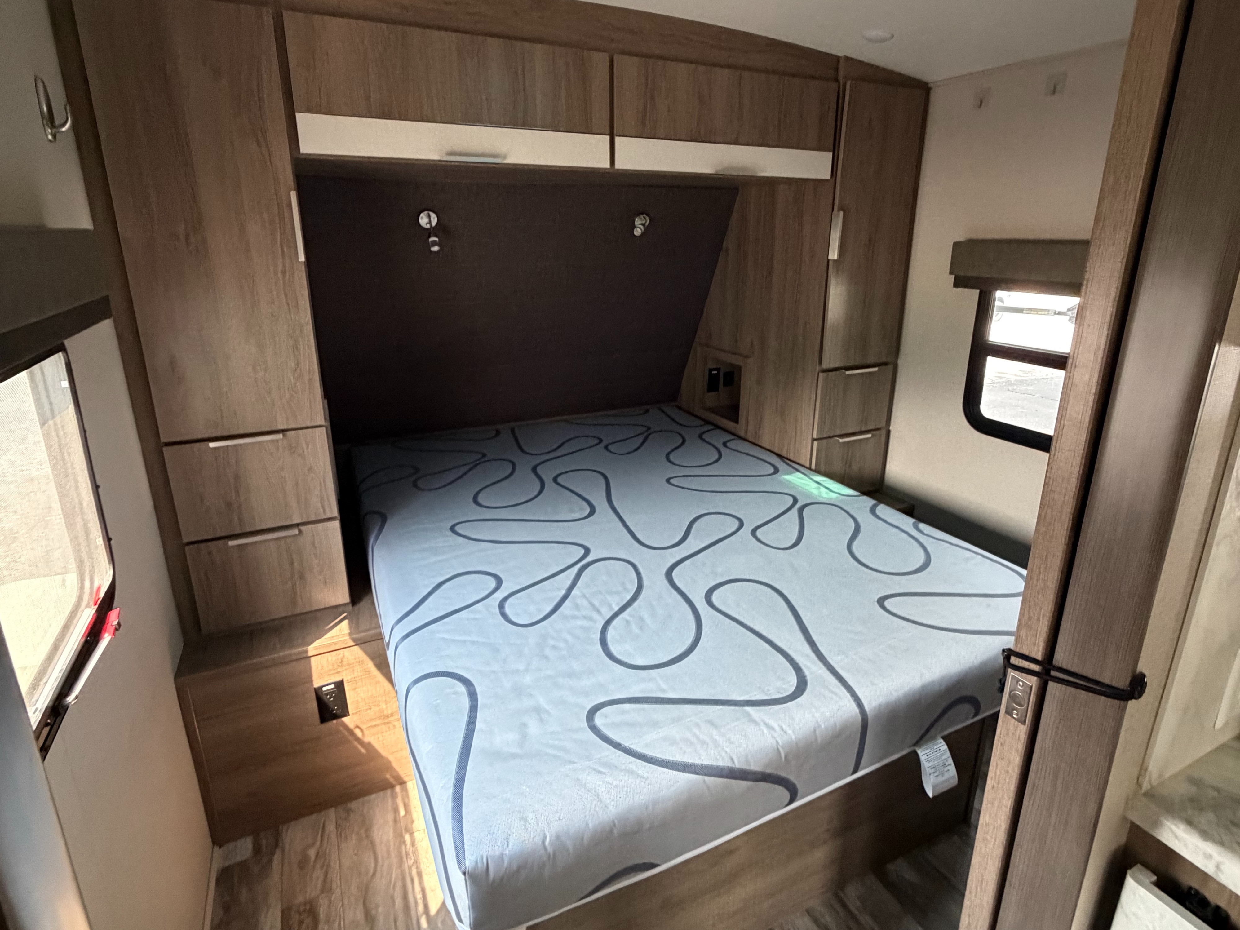 RV rental's compact bedroom features a patterned mattress, built-in storage, and side windows for a comfortable stay.. Grand Design Imagine 2021