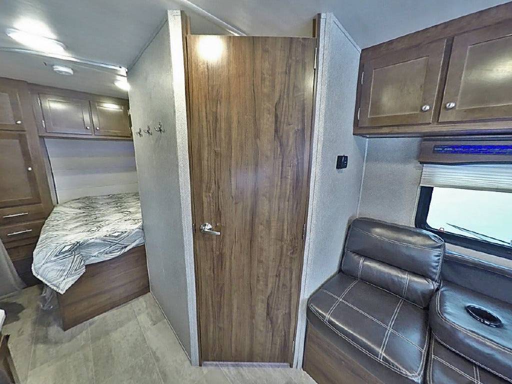 RV rental interior: cozy bed with patterned comforter, wood cabinets, and a comfy dark sofa with cup holders by a window.. Heartland RVs Terry Classic 2019