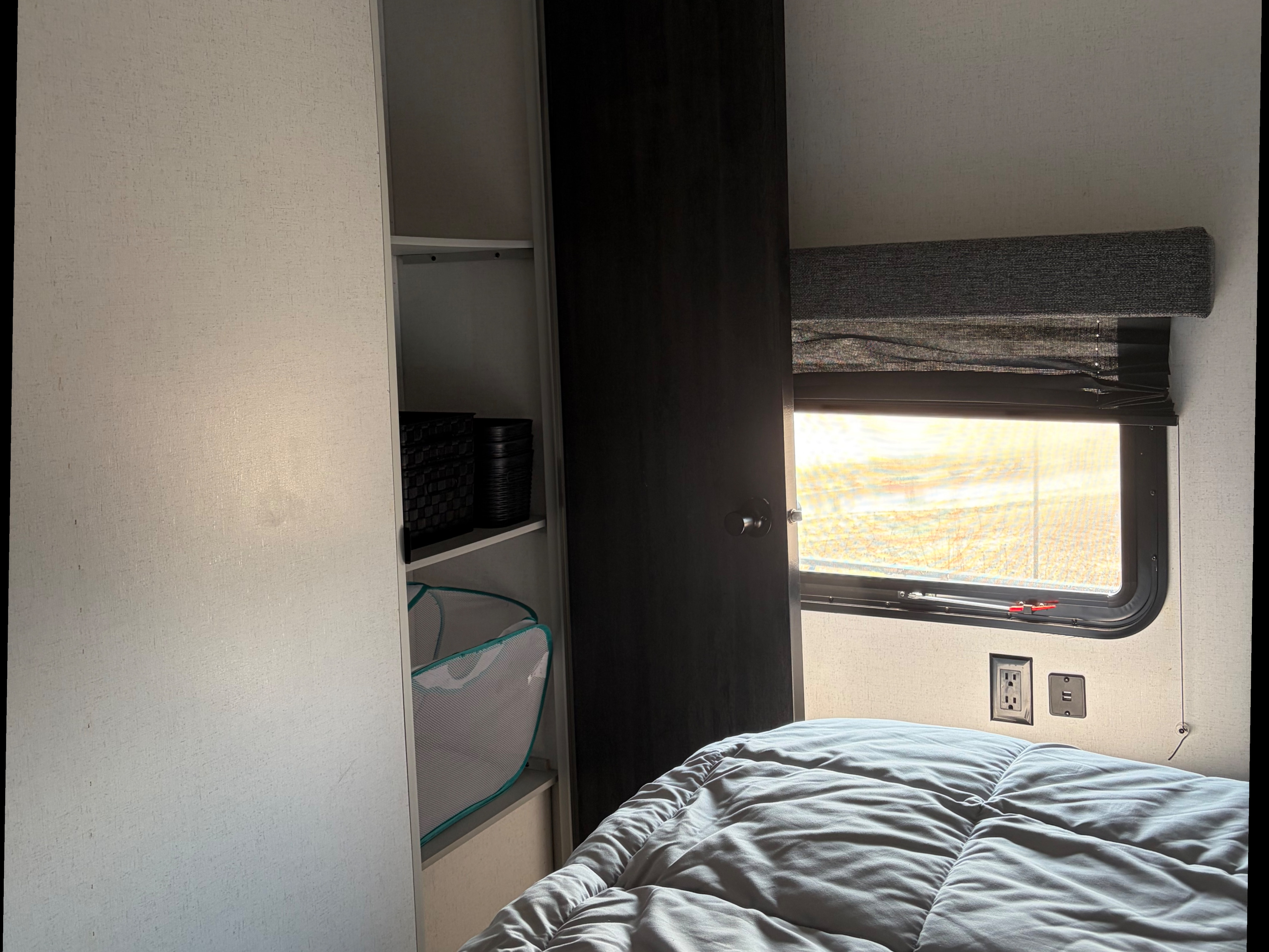 RV rental bedroom interior: a comfy bed, sunlit window with shades, and open wardrobe shelving with storage items.. Forest River Salem 2022