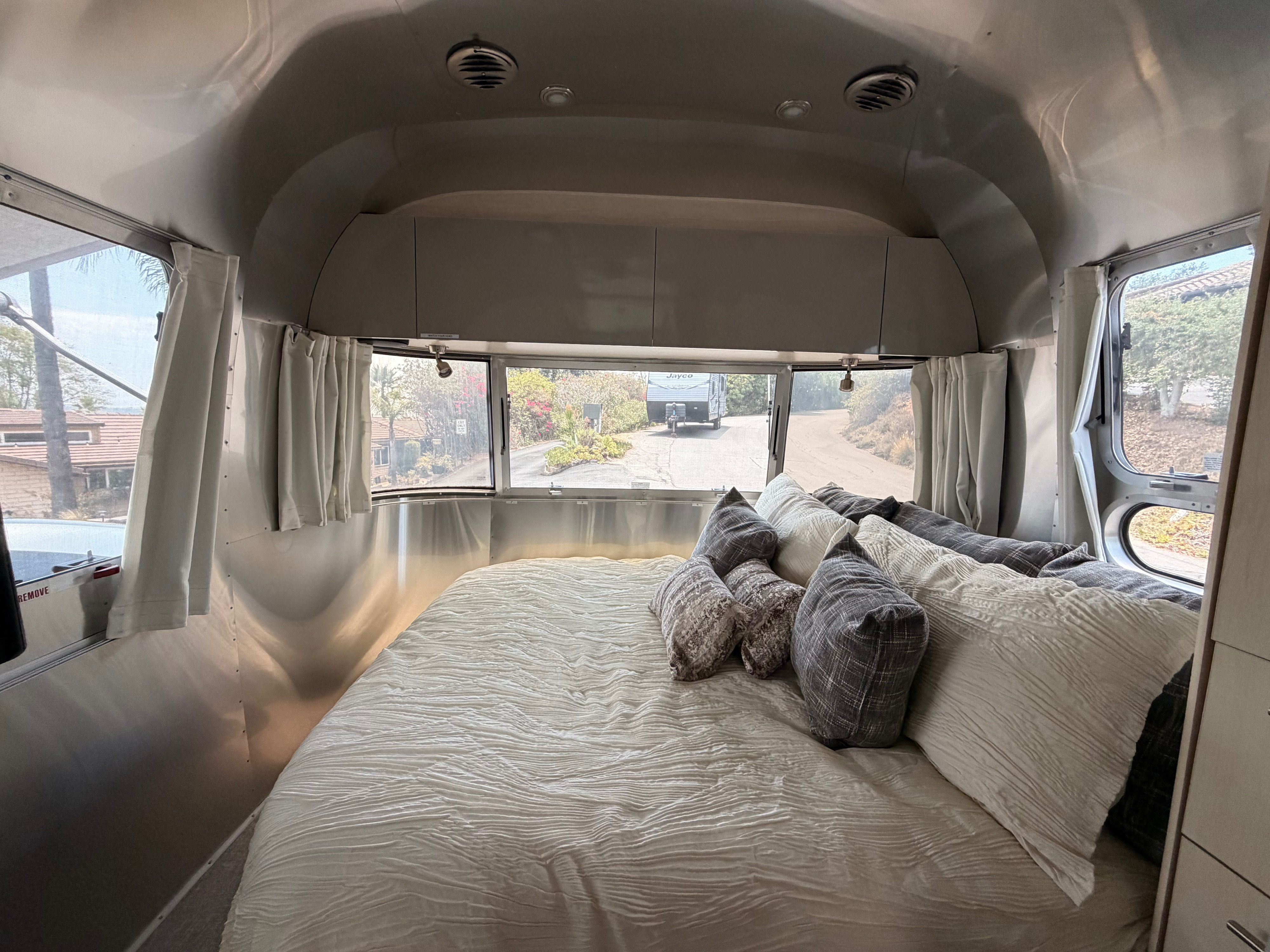 Cozy RV rental bedroom with a comfortable bed, metallic walls, and expansive windows offering scenic outdoor views.. Airstream Flying Cloud 2022