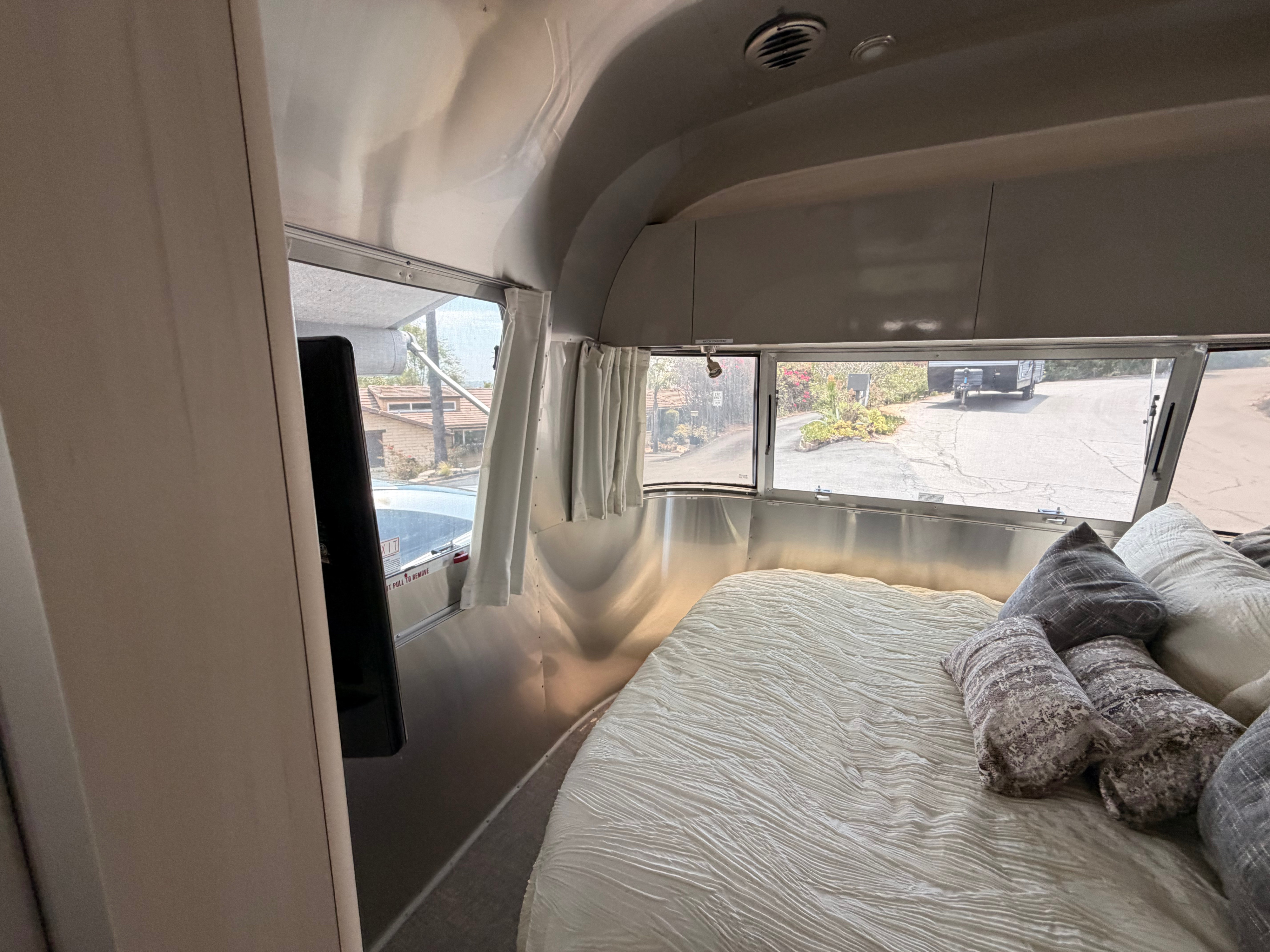Gleaming Airstream rv rental bedroom with a plush bed, white textured bedding, gray pillows, and panoramic windows.. Airstream Flying Cloud 2022