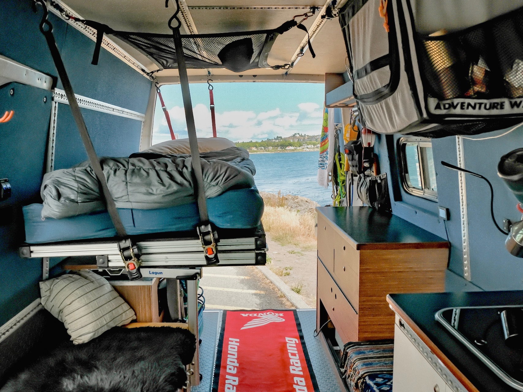 Adventure-ready rv rental camper van interior. Features a bed, kitchen, and open rear doors overlooking the ocean.. Mercedes-Benz Sprinter 2006