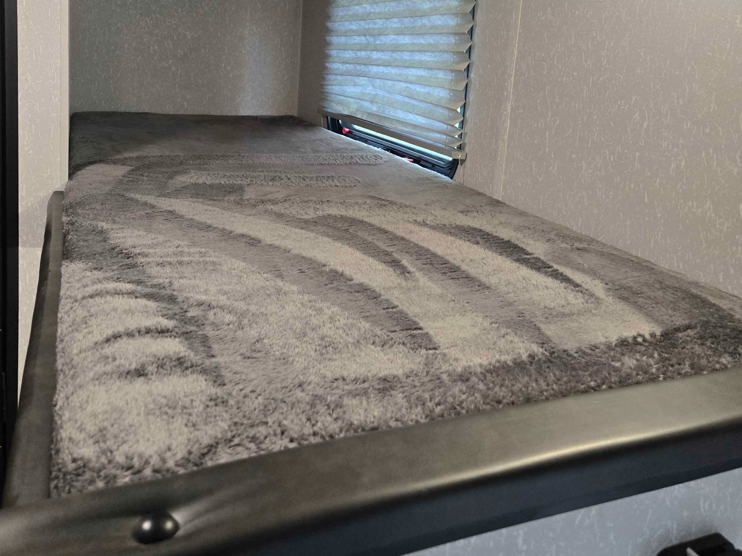 Cozy RV rental bunk bed with a soft grey patterned blanket and a pleated window shade, perfect for sleeping.. Forest River Cherokee Wolf Pup 2022