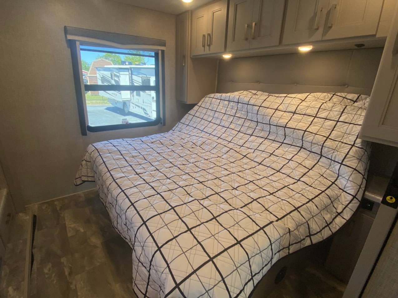 Spacious RV rental bedroom featuring a large bed, window with an exterior view, and convenient overhead cabinets.. Thor Challenger 2024