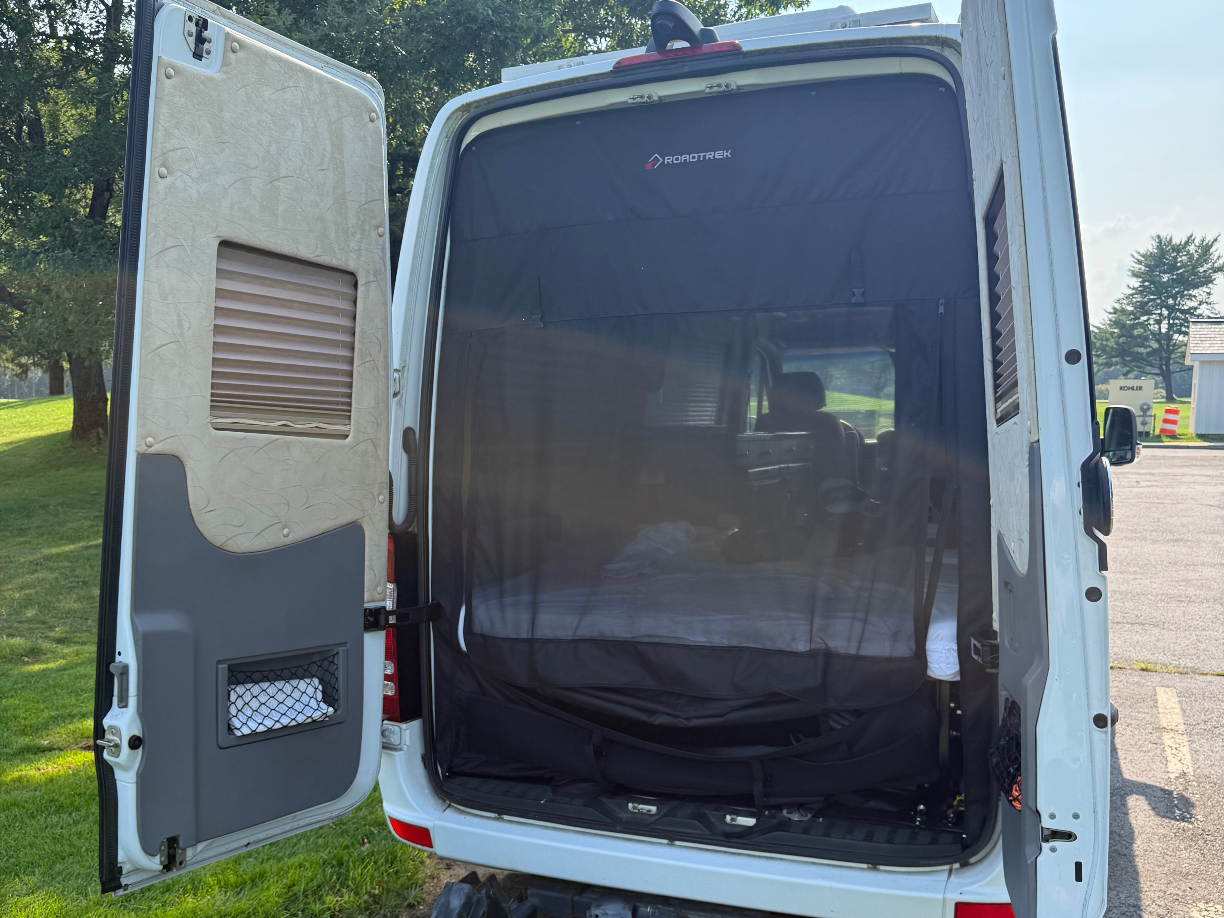 Open rear doors of an rv rental Roadtrek camper van, revealing a bug screen & comfortable interior bed.. Roadtrek Roadtrek Class B 2014