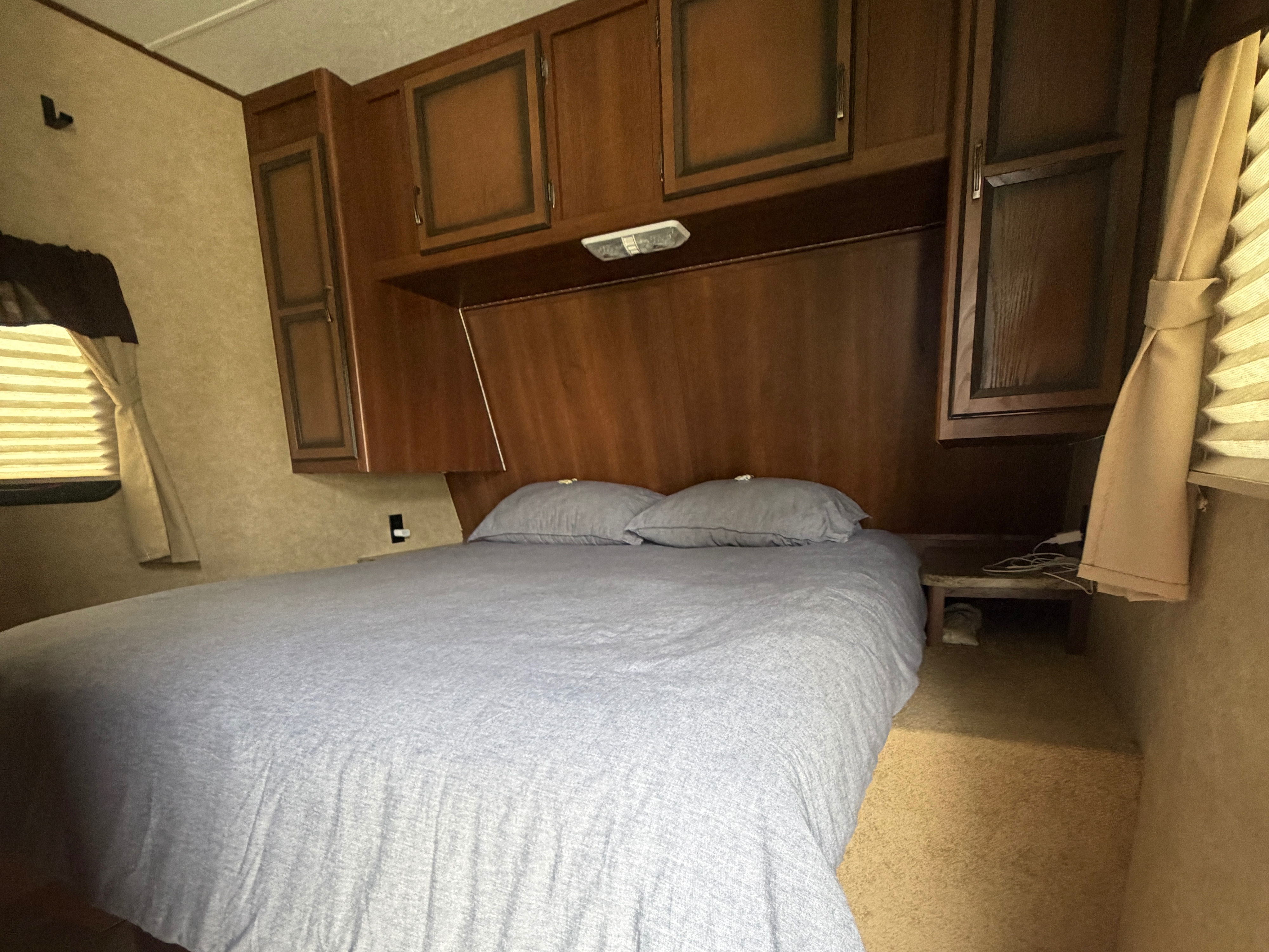Bedroom in an RV rental featuring a comfy bed, wooden storage cabinets, and a window with blinds.. Crossroads RV Zinger 2014
