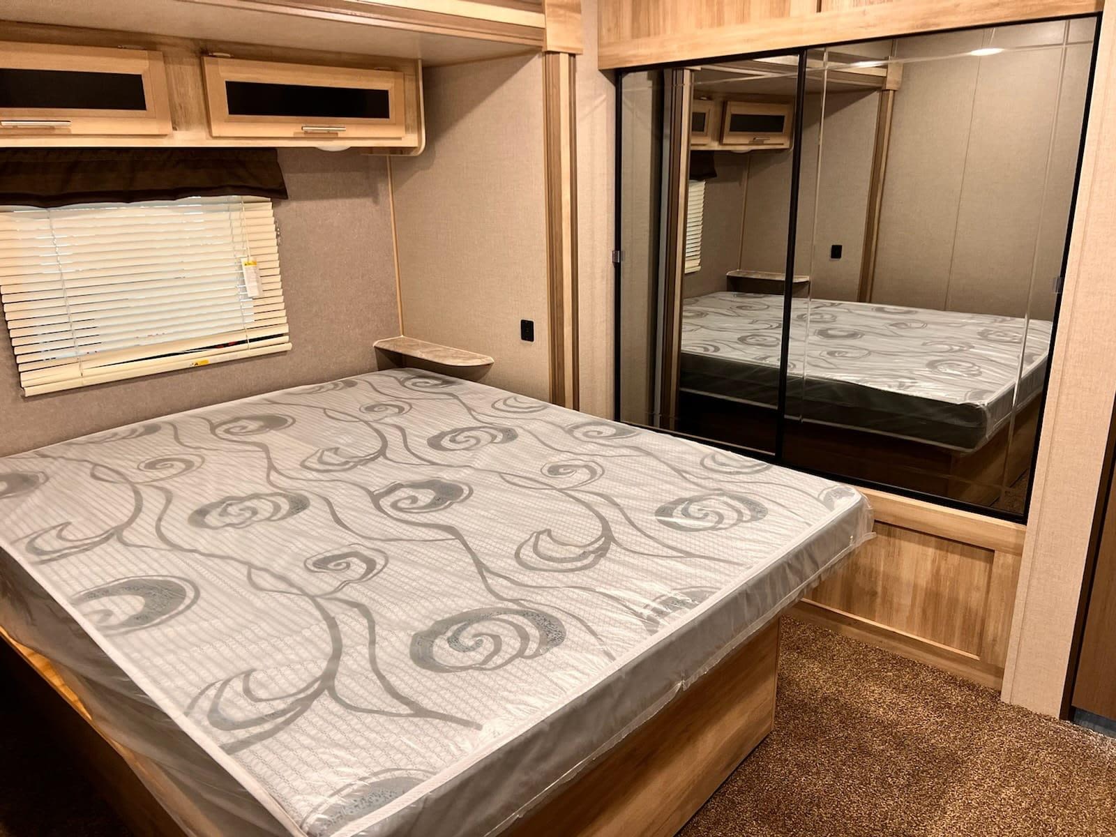 Clean RV rental bedroom features a new, plastic-covered mattress, window, and mirrored closet for guests.. Coachmen Catalina 2022