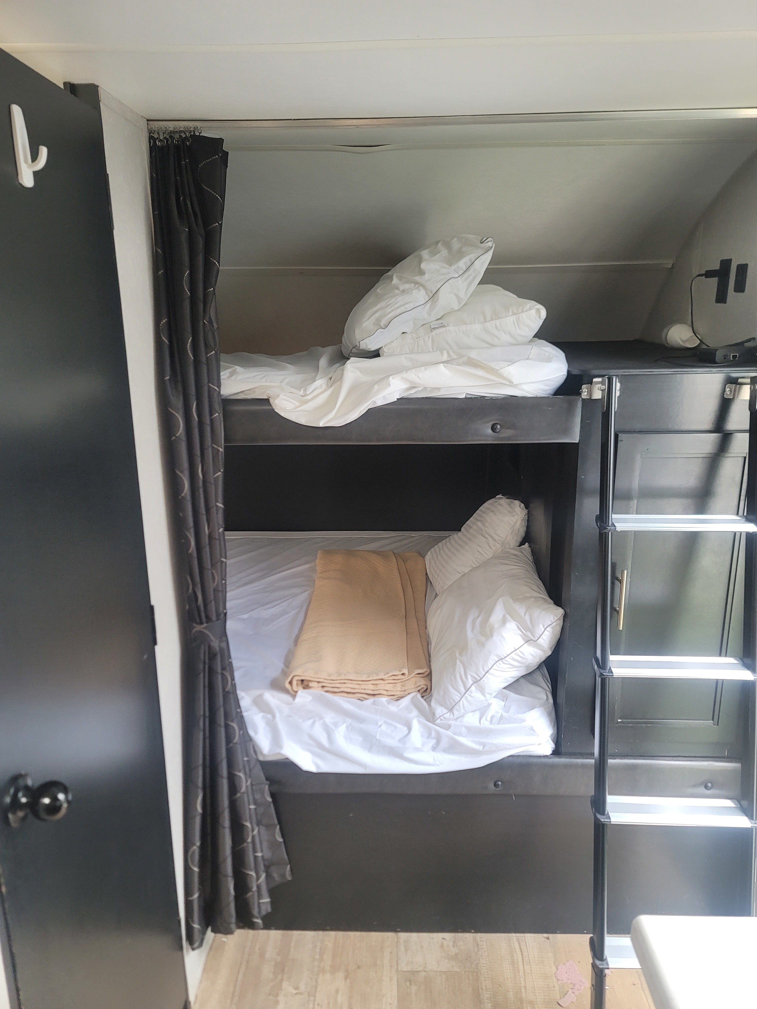 Inside an RV rental, a set of bunk beds with white linens, pillows, and a folded blanket, complete with a privacy curtain.. Forest River GRAY WOLF 2021