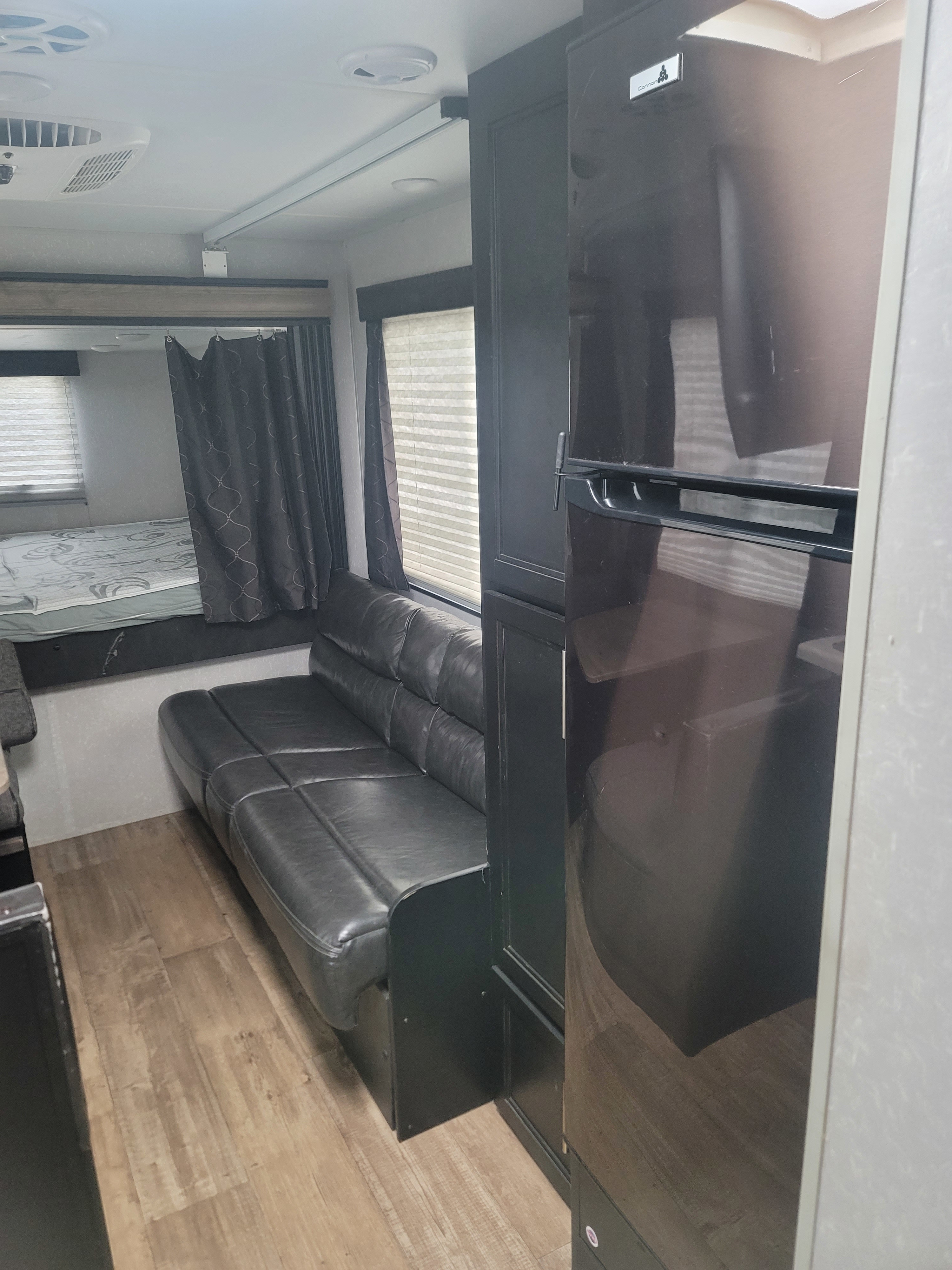 Inside an RV rental: view of a black sofa, bunk bed with curtains, and dark refrigerator unit. Ready for travel!. Forest River GRAY WOLF 2021