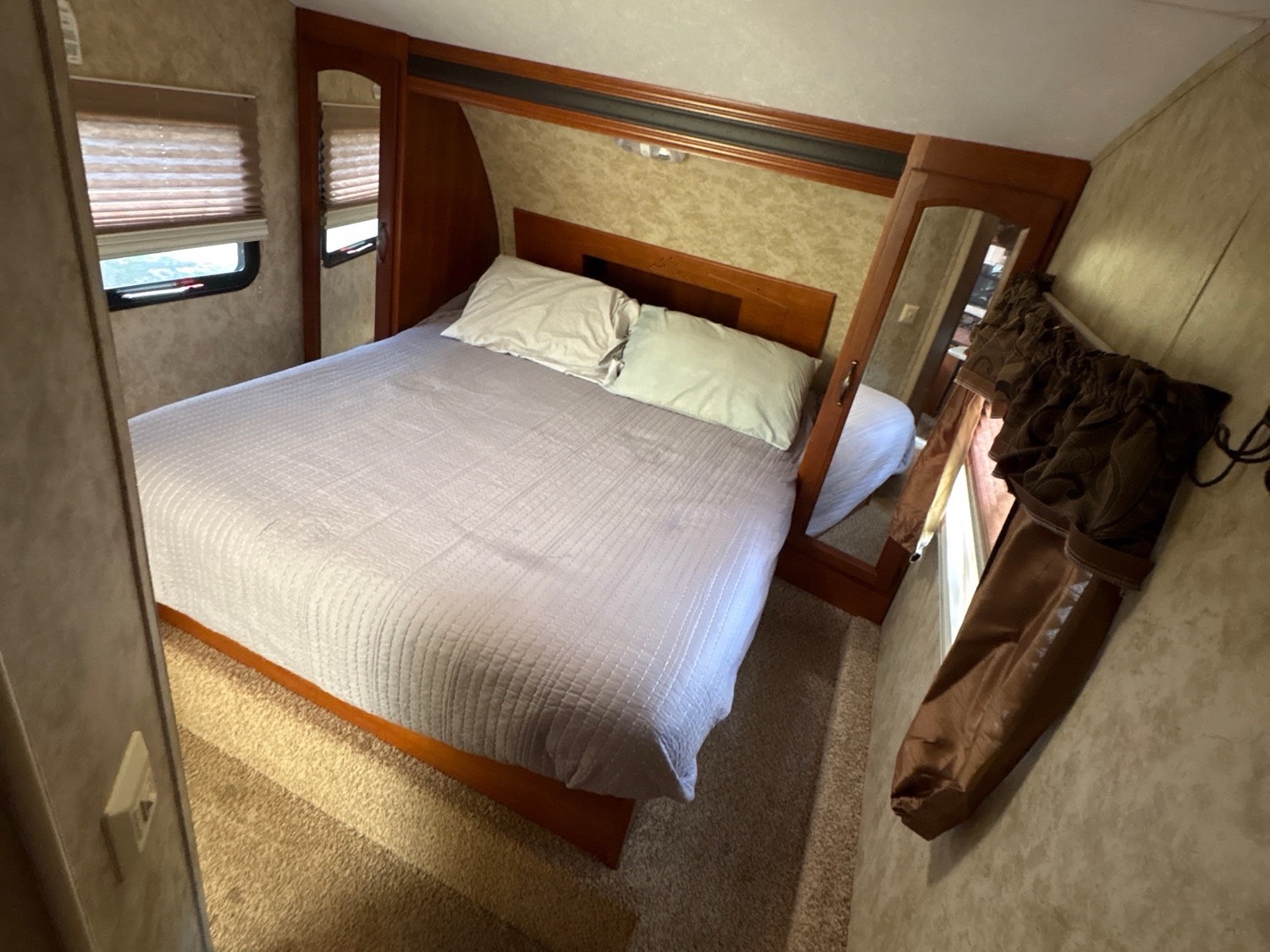 Cozy bedroom in an RV rental, featuring a queen bed, window with blinds, and mirrored wardrobe.. Keystone RV Cougar 2013