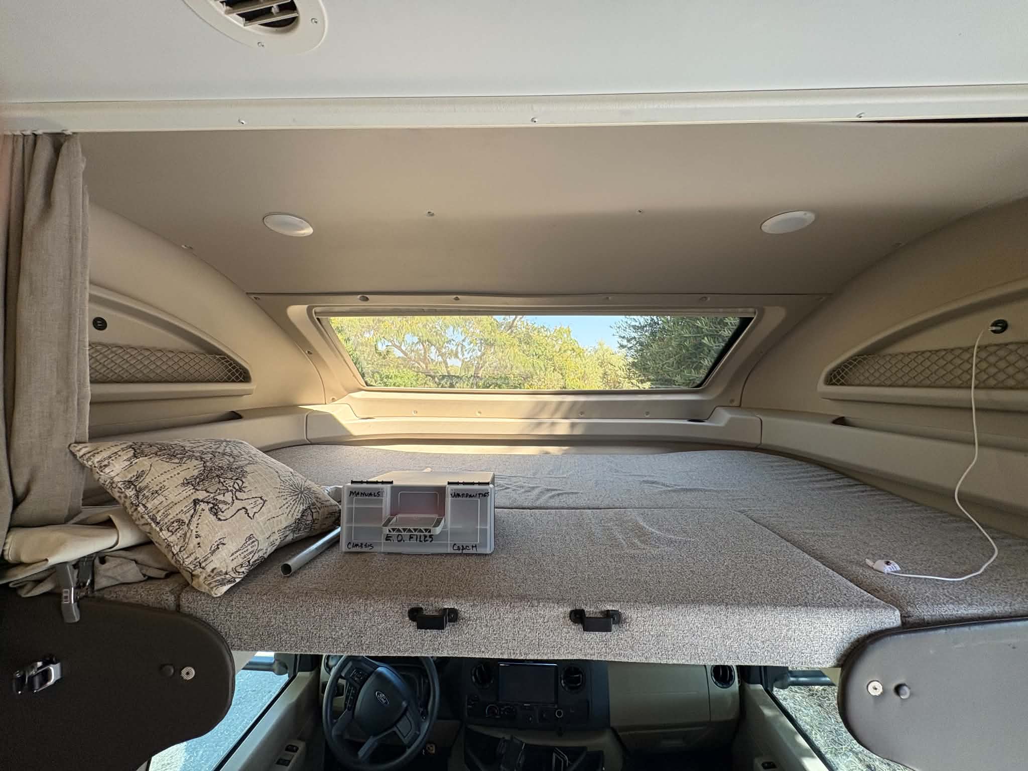 Cozy RV rental cab-over bunk with organizer & dashboard visible below. Ready for your motorhome travel adventures.. Entegra Coach Odyssey 2021