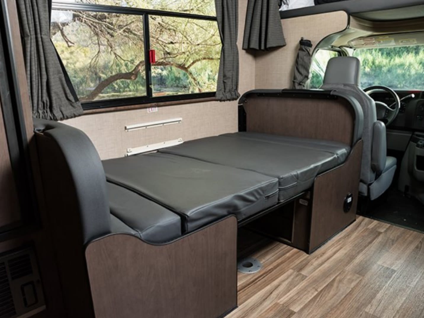Inside this RV rental, comfy dark grey seating transforms into a bed, with a scenic window view and driver's area.. Thor Majestic 2019