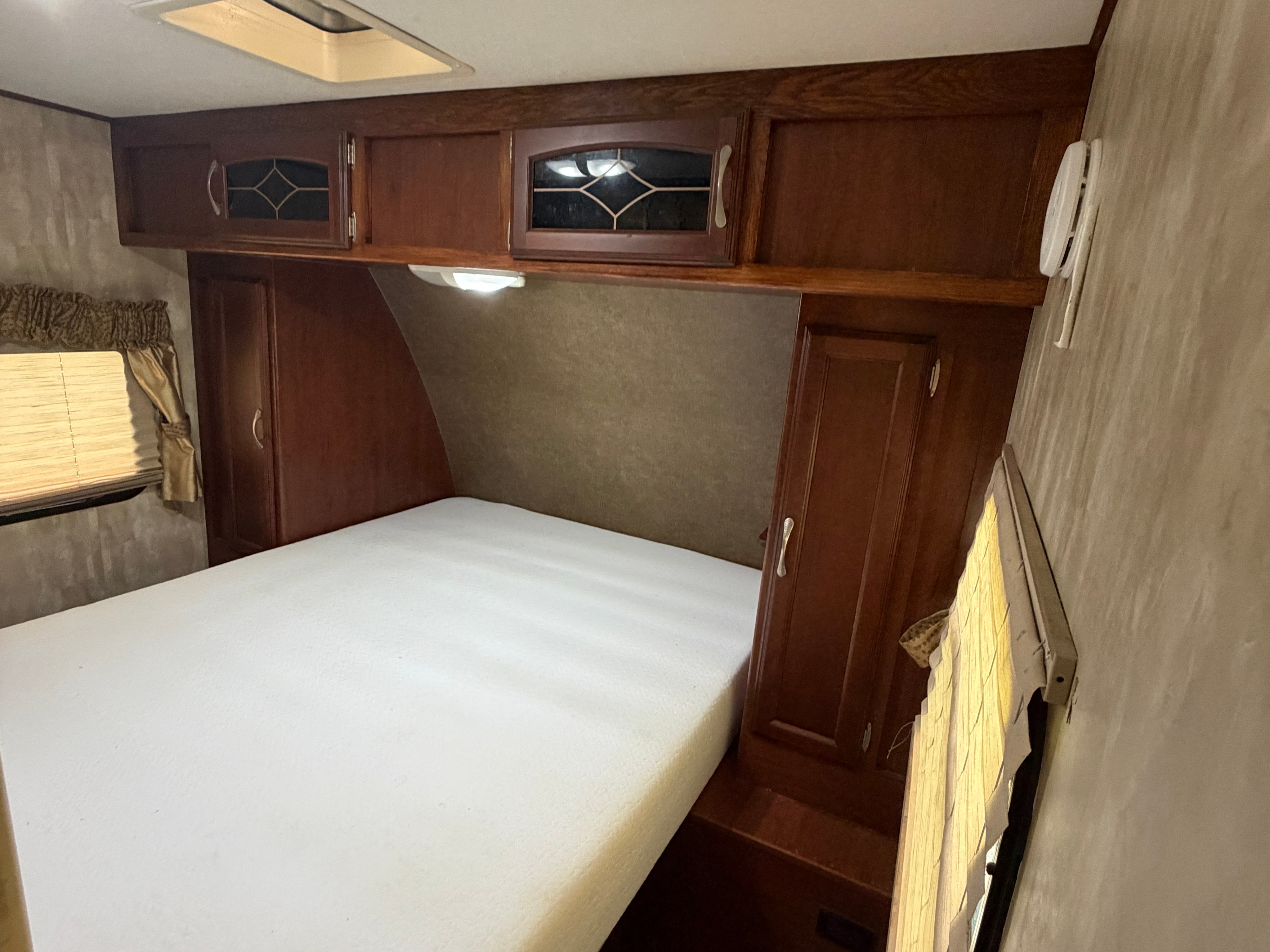 Cozy RV rental bedroom with a comfortable white mattress, wooden cabinetry, and window blinds. Ideal for travel.. Winnebago Minnie Winnie 2015