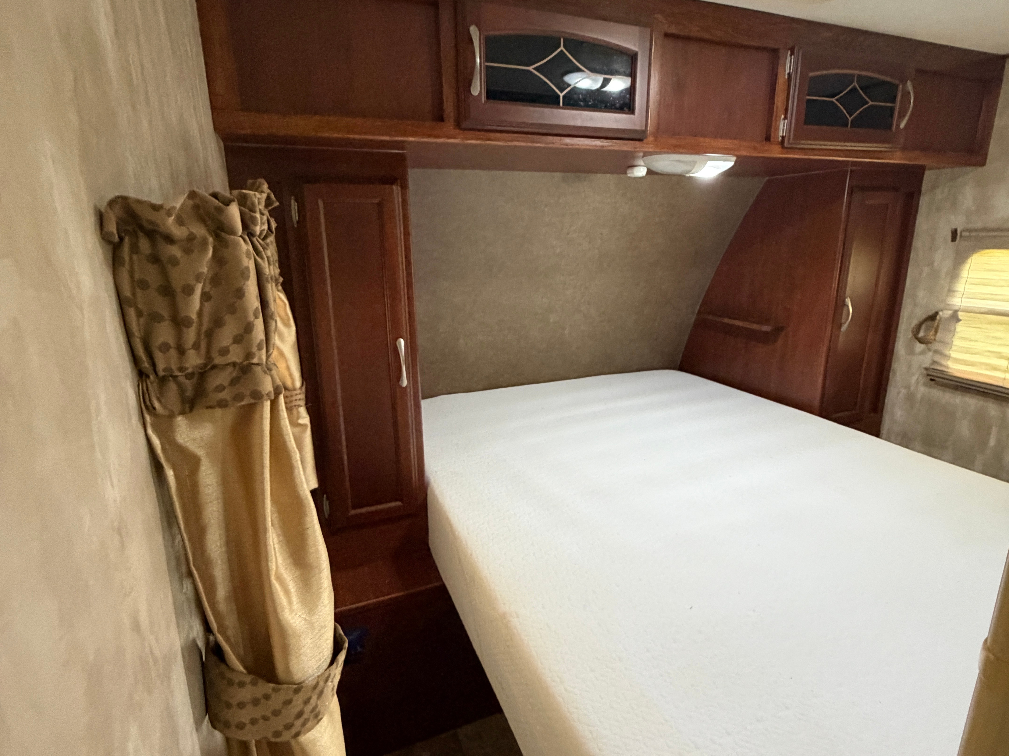 Inside an RV rental: a compact bedroom with a white bed, overhead storage, and side cabinets, offering a cozy sleeping space.. Winnebago Minnie Winnie 2015