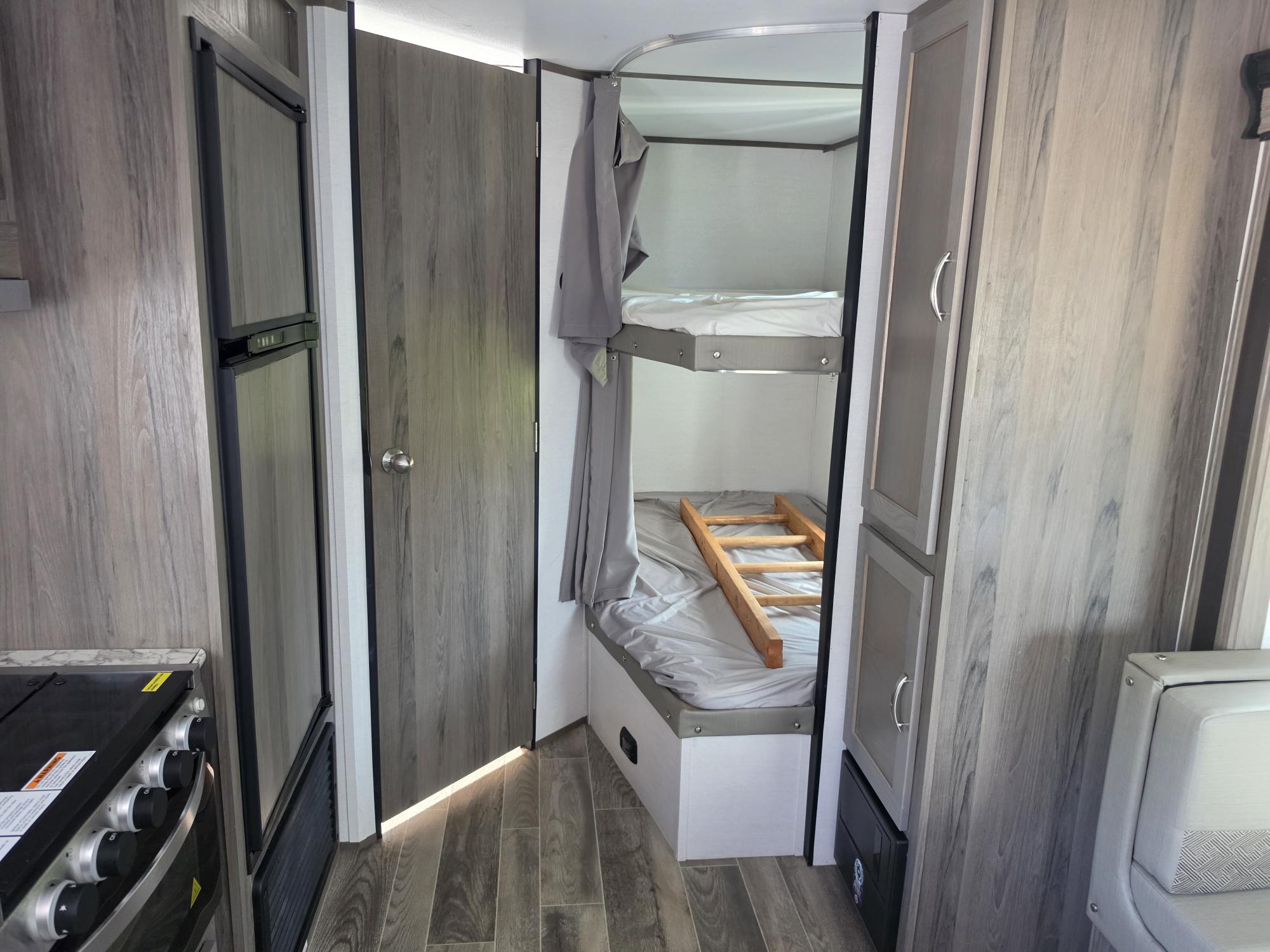 Inside a modern rv rental: bunk beds, a ladder, kitchenette with a fridge and stove, and light wood-look interior accents.. Gulf Stream Envision 2025
