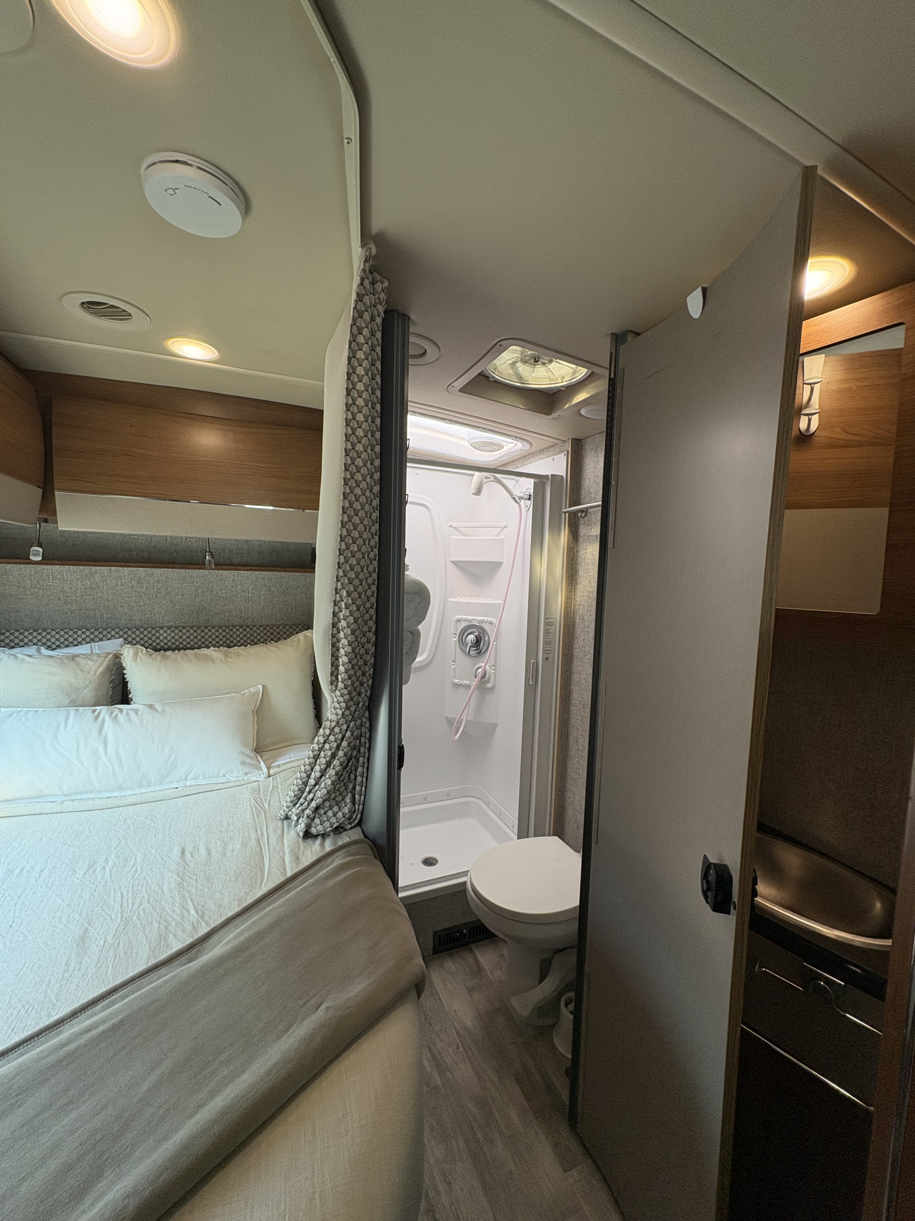 Inside an **rv rental**, a compact space features a cozy bed with light bedding, and a full bathroom with a shower and toilet.. Winnebago Navion 2017