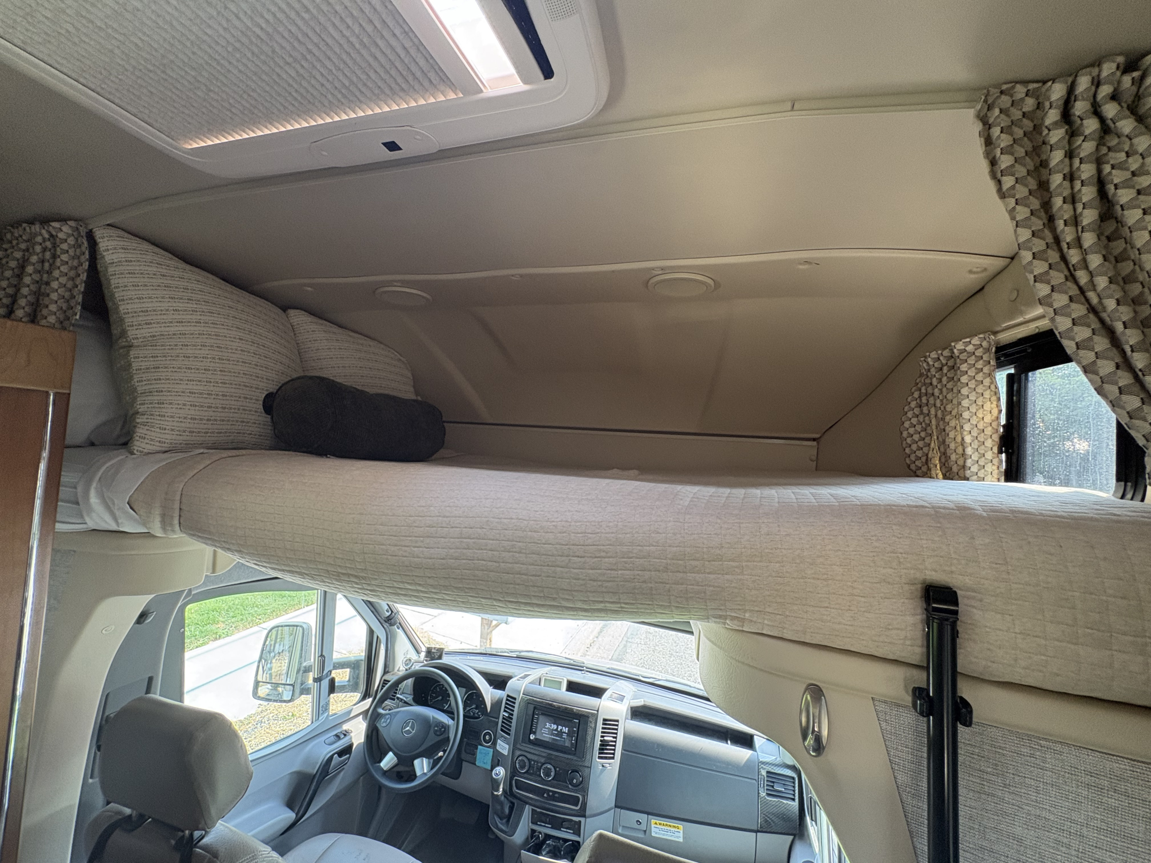 Inside this rv rental, a comfortable overhead bed is positioned above the driver's cockpit of a camper van, ready for travel.. Winnebago Navion 2017