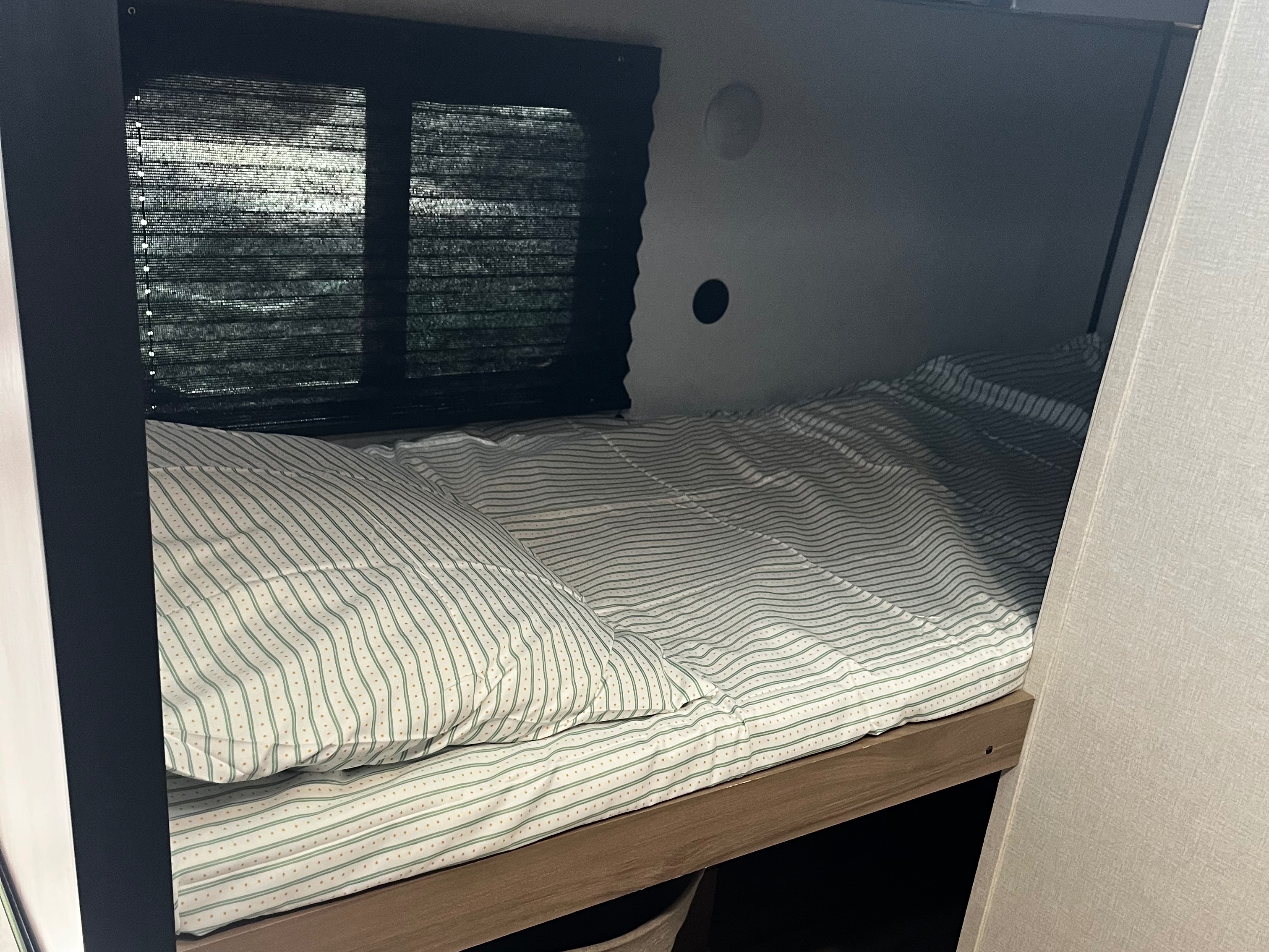 Cozy RV rental bunk bed with striped bedding, window blinds, and interior light. Ideal for comfortable RV travel.. Keystone RV Coleman 2025
