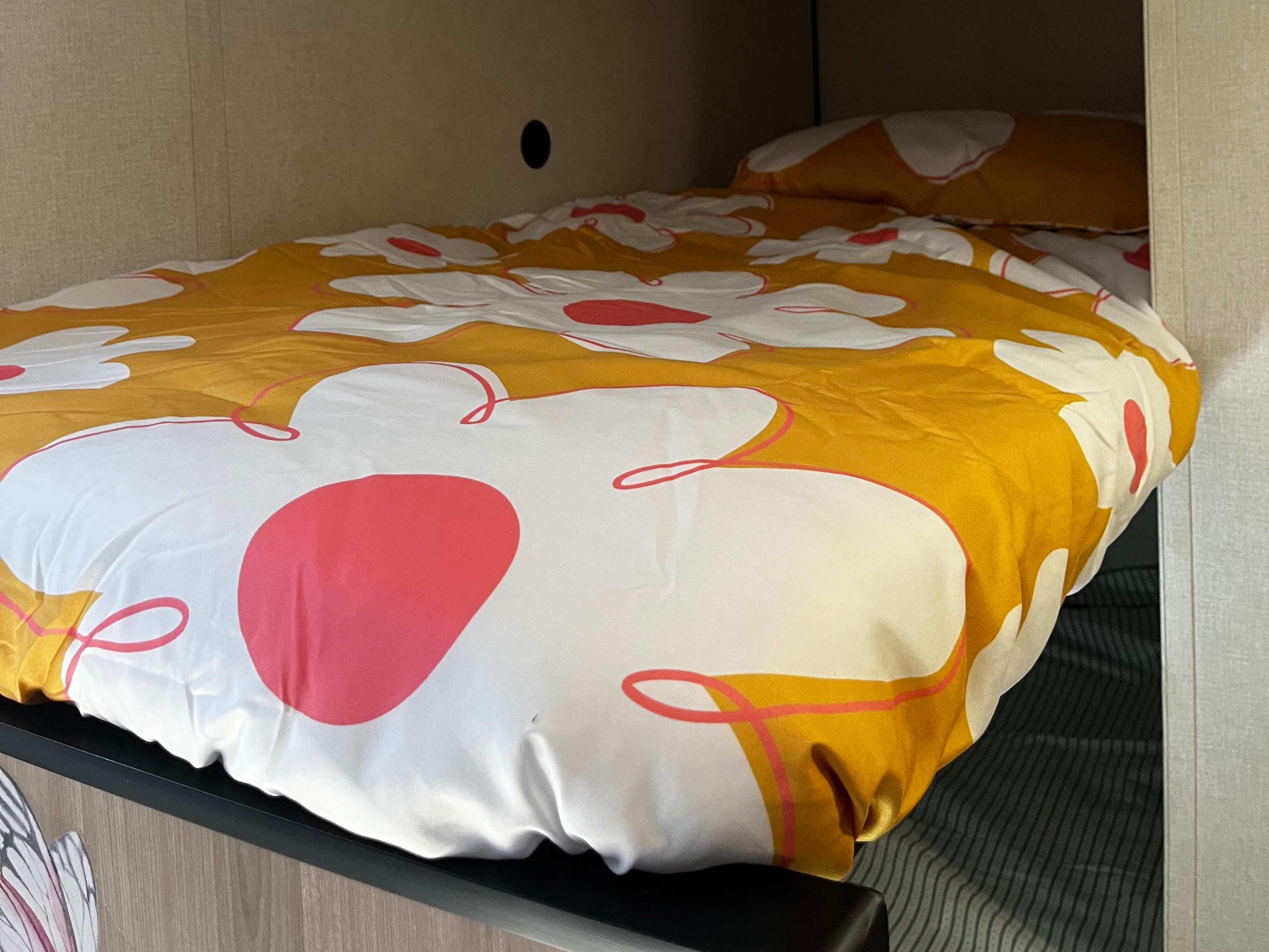 Cozy bunk bed in an RV rental, featuring vibrant yellow, white, and red floral bedding and a small vent on the wall.. Keystone RV Coleman 2025