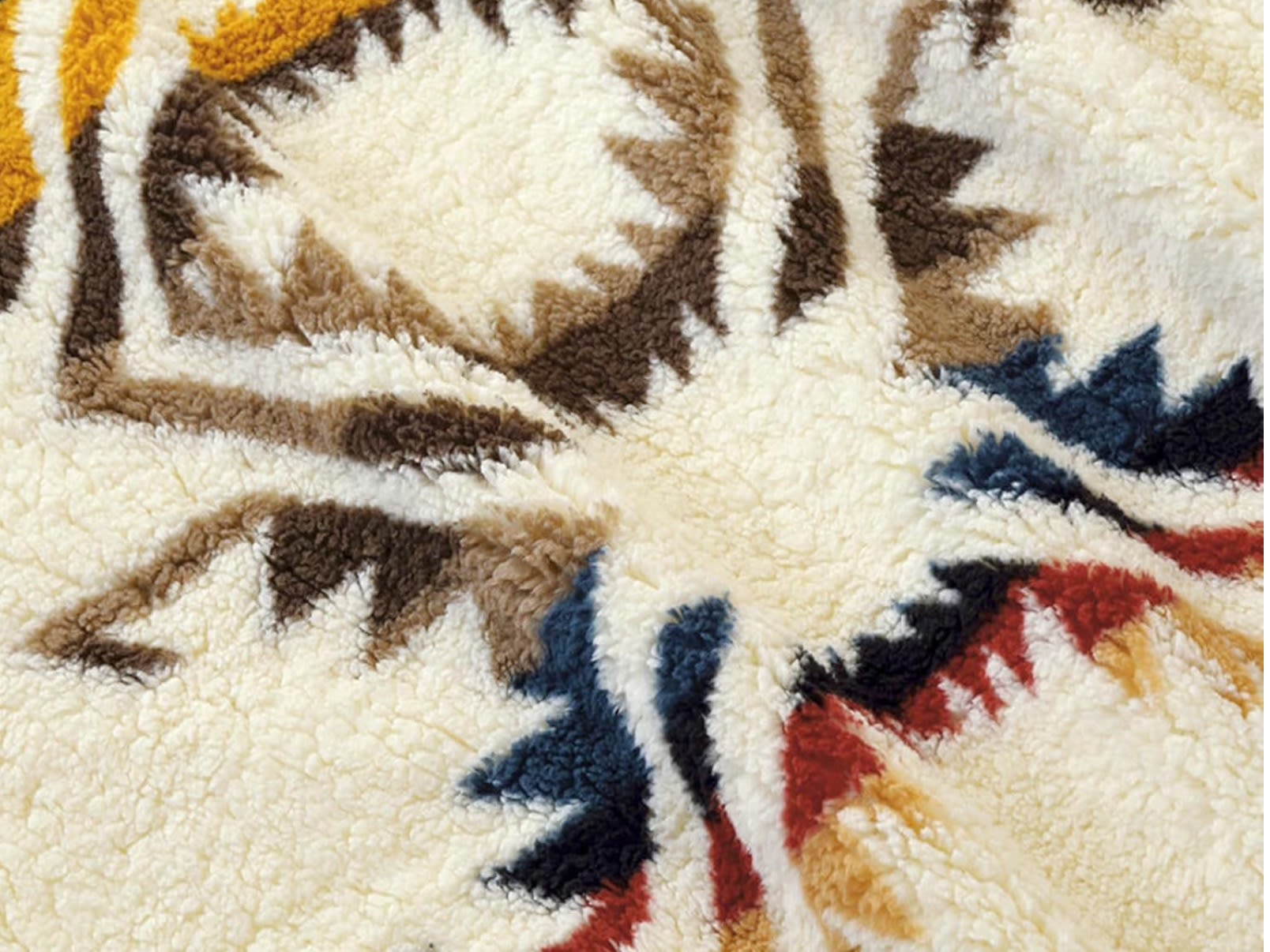 Close-up: fluffy patterned blanket with cream, brown, blue, red, & yellow accents. Perfect for an RV rental.. Airstream Bambi 2021