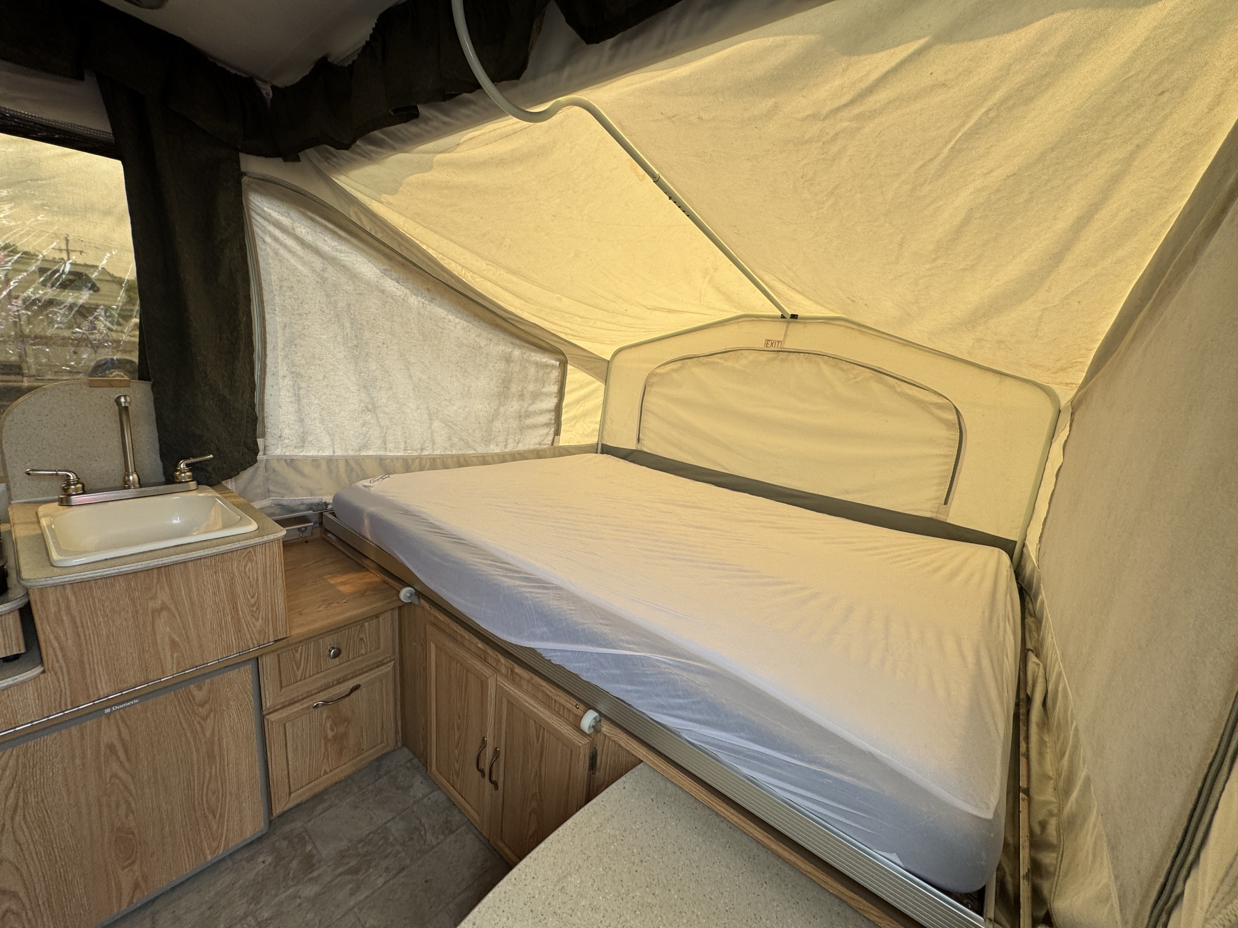 RV rental interior featuring a cozy pop-up camper bed, compact sink, and wooden cabinets, ideal for travelers.. Forest River Yearlying 4100 2008